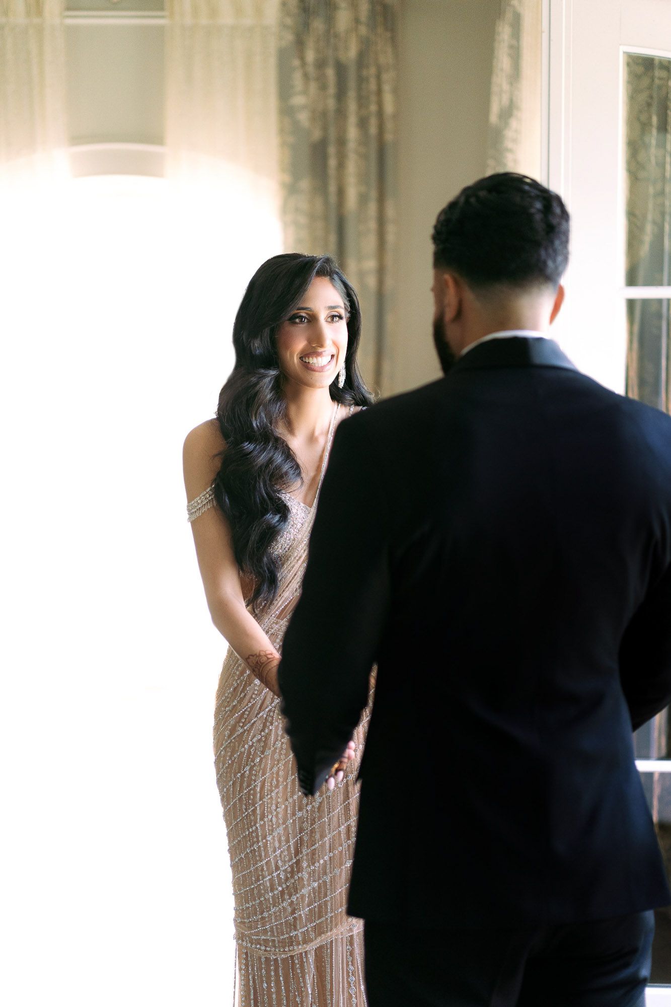 A woman in a beaded dress stands near a window while a man in a dark suit is seen from behind.
