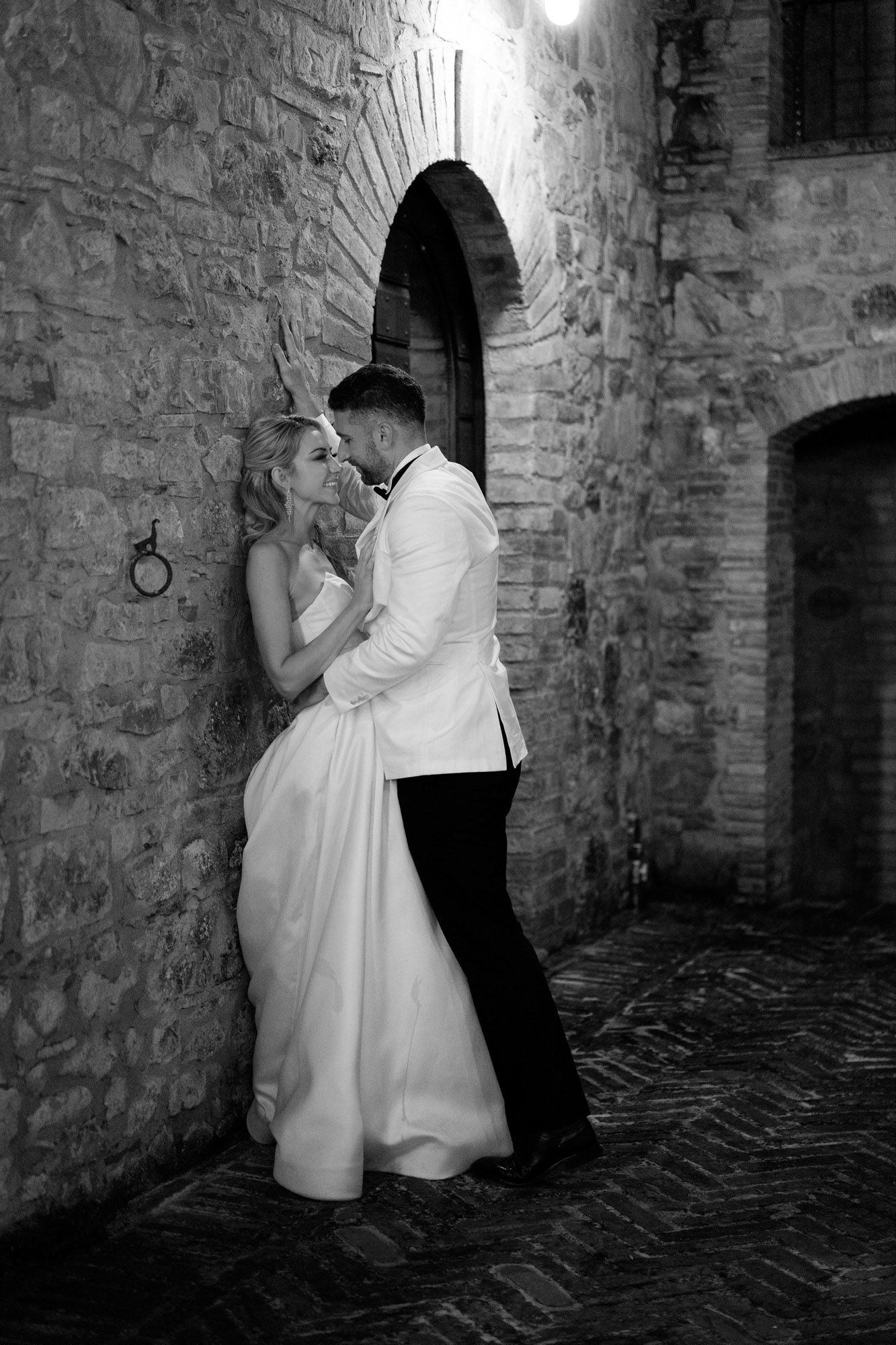 A romantic black and white photo series showing a couple in wedding attire embracing against a stone wall.