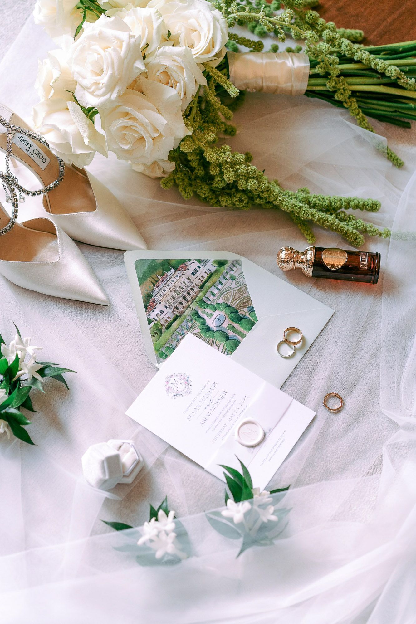 Wedding details flatlay with white roses, invitation cards, rings and bridal shoes on light fabric background.