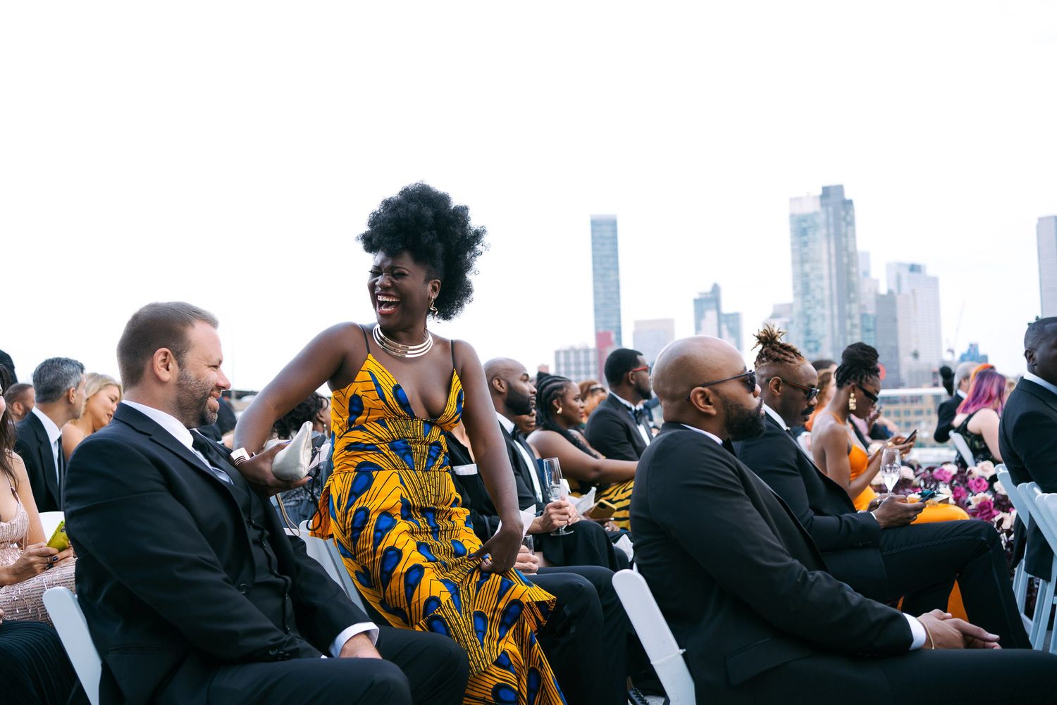 People gather at a rooftop venue with city skyline views while enjoying drinks and conversation.