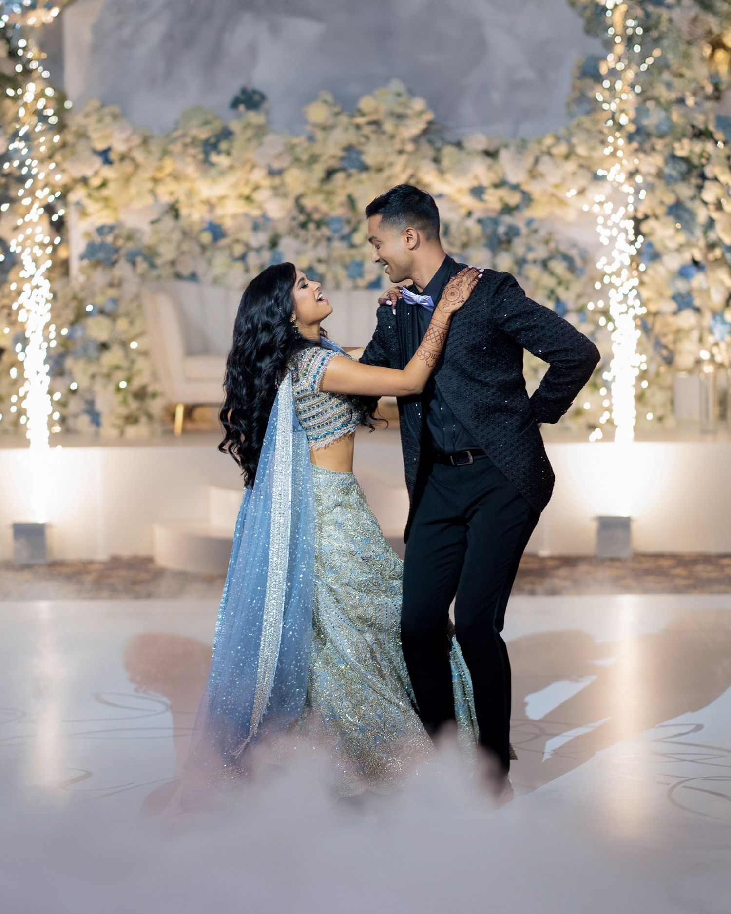 Two dancers perform a graceful ballroom dance sequence in front of an ornate floral backdrop.