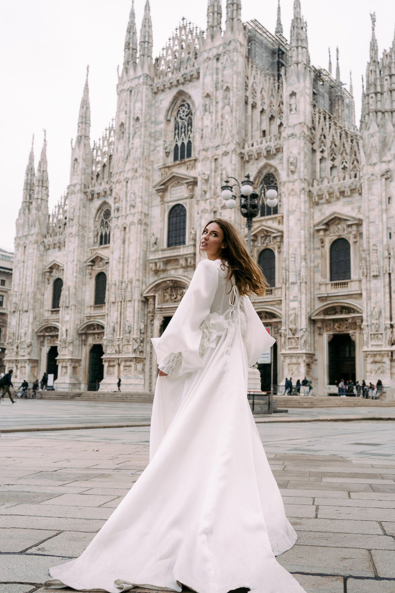A flowing white dress twirls gracefully in front of the historic Milan Cathedral's ornate Gothic facade.