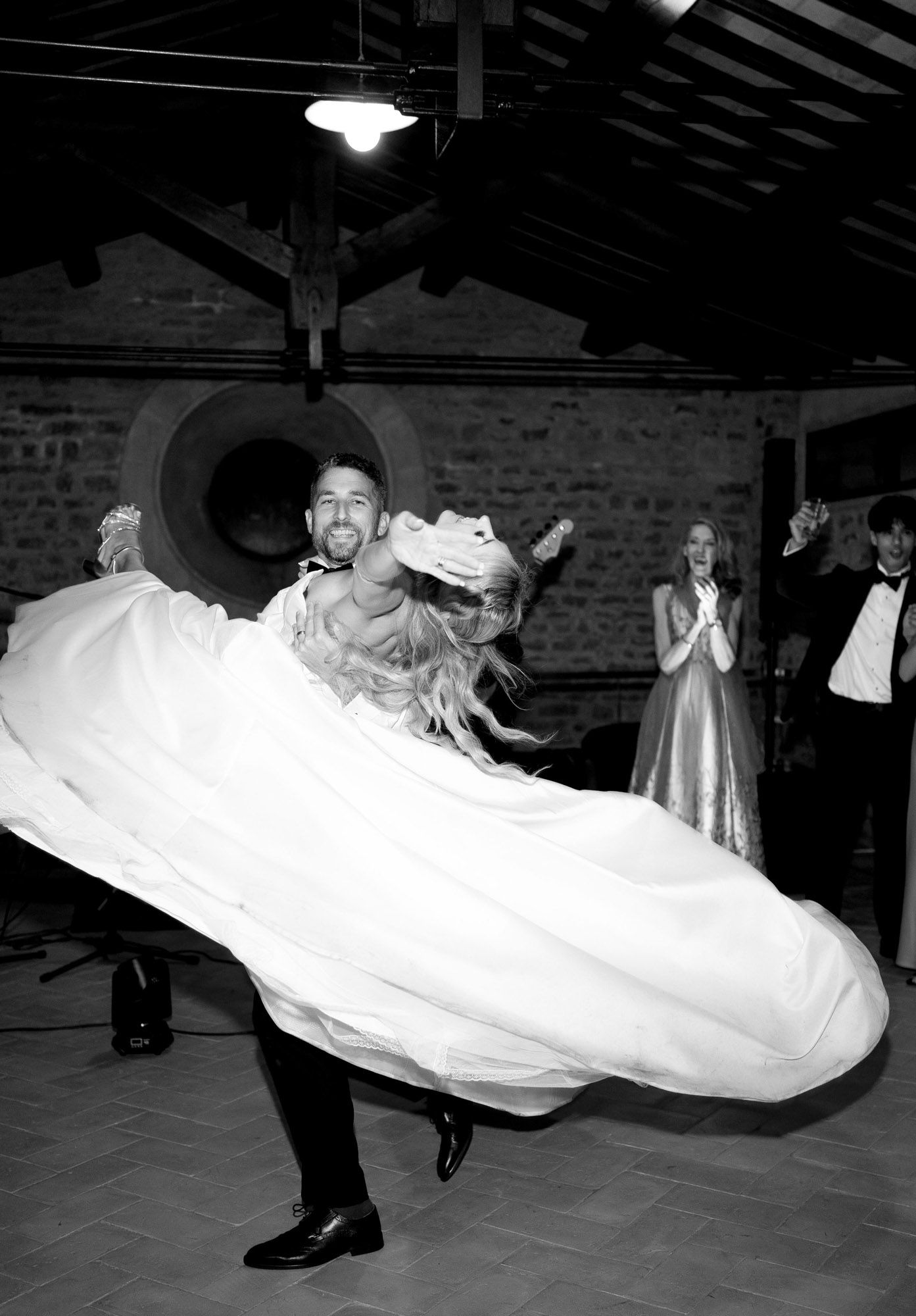 A black and white photo of a couple dancing at their wedding reception, with the bride's dress swirling dramatically.
