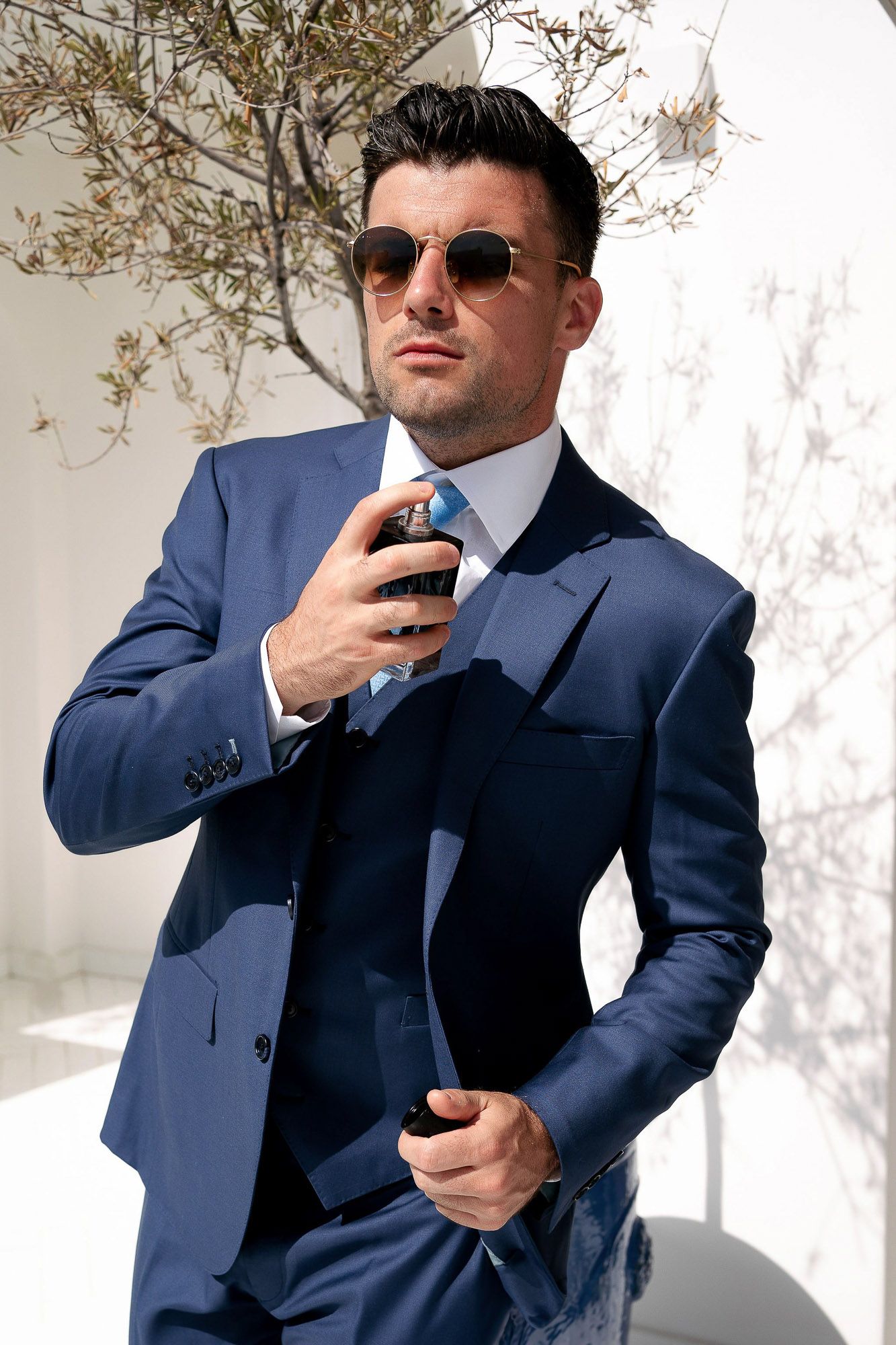 Professional in navy blue suit and sunglasses poses with phone in three similar shots against white background.