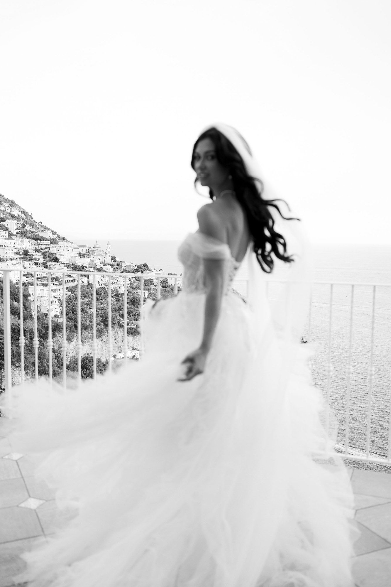 Flowing white wedding dress twirling in motion against a bright coastal backdrop.