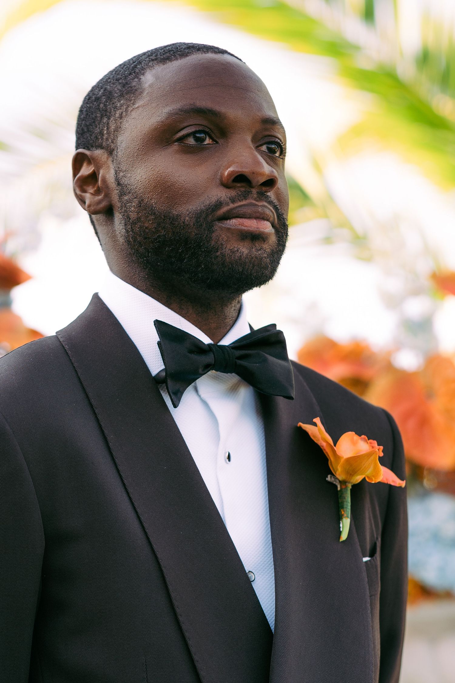Formal black tuxedo with orange boutonniere in outdoor wedding setting.