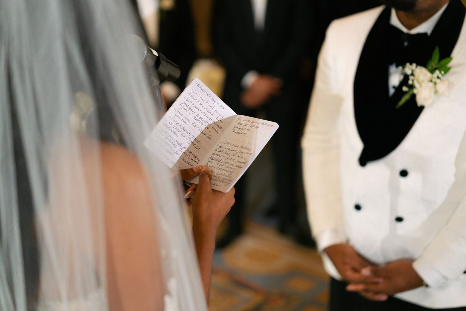 A wedding party stands together during a ceremony while holding ceremony programs and wearing formal attire.