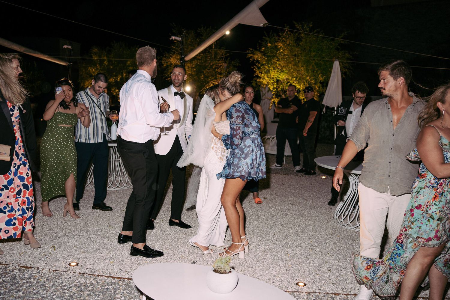 People dancing and socializing at an outdoor evening event on a gravel or stone surface.