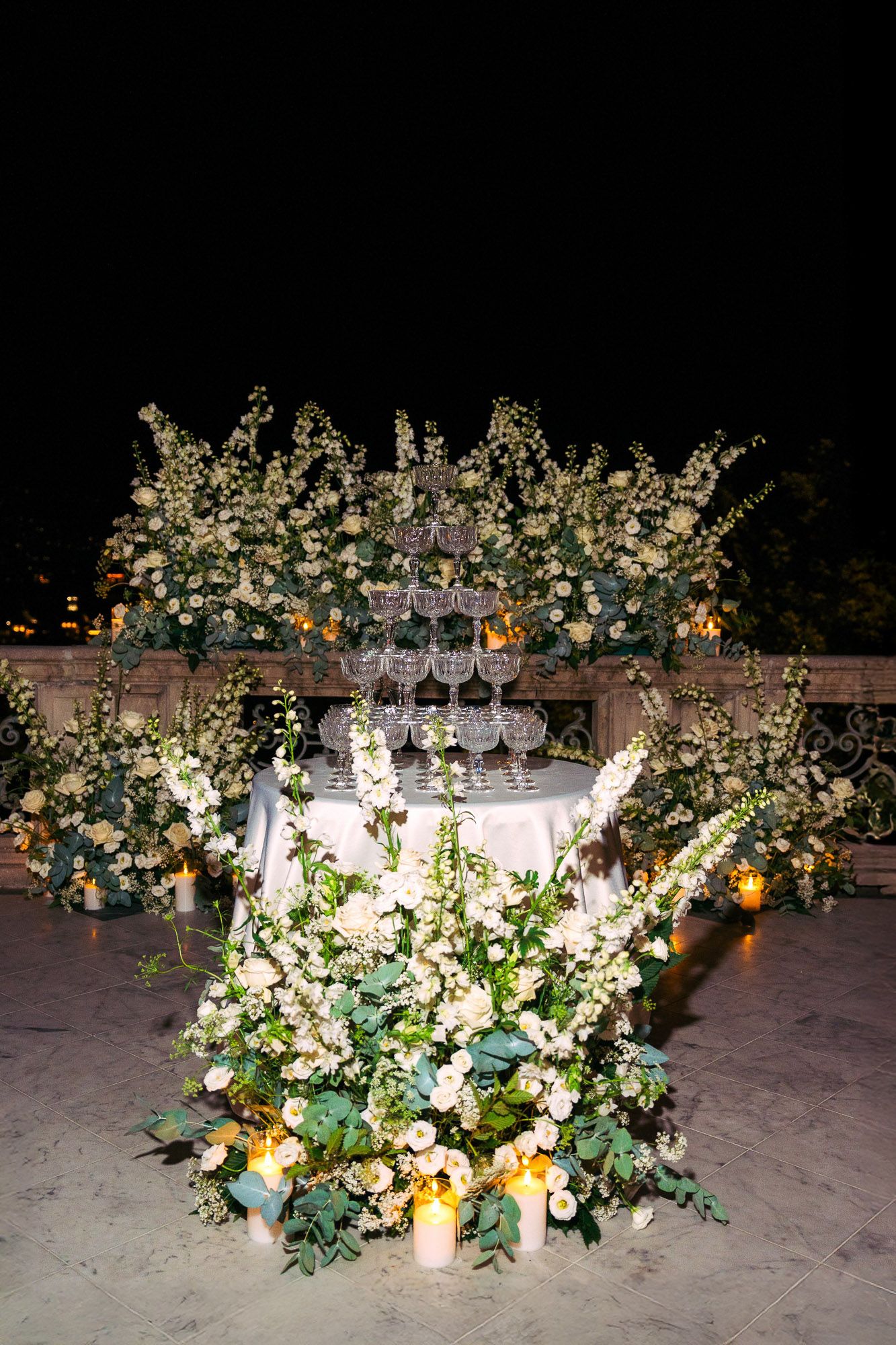 Elegant floral table arrangements with white blooms and greenery illuminated by candlelight at a wedding reception.