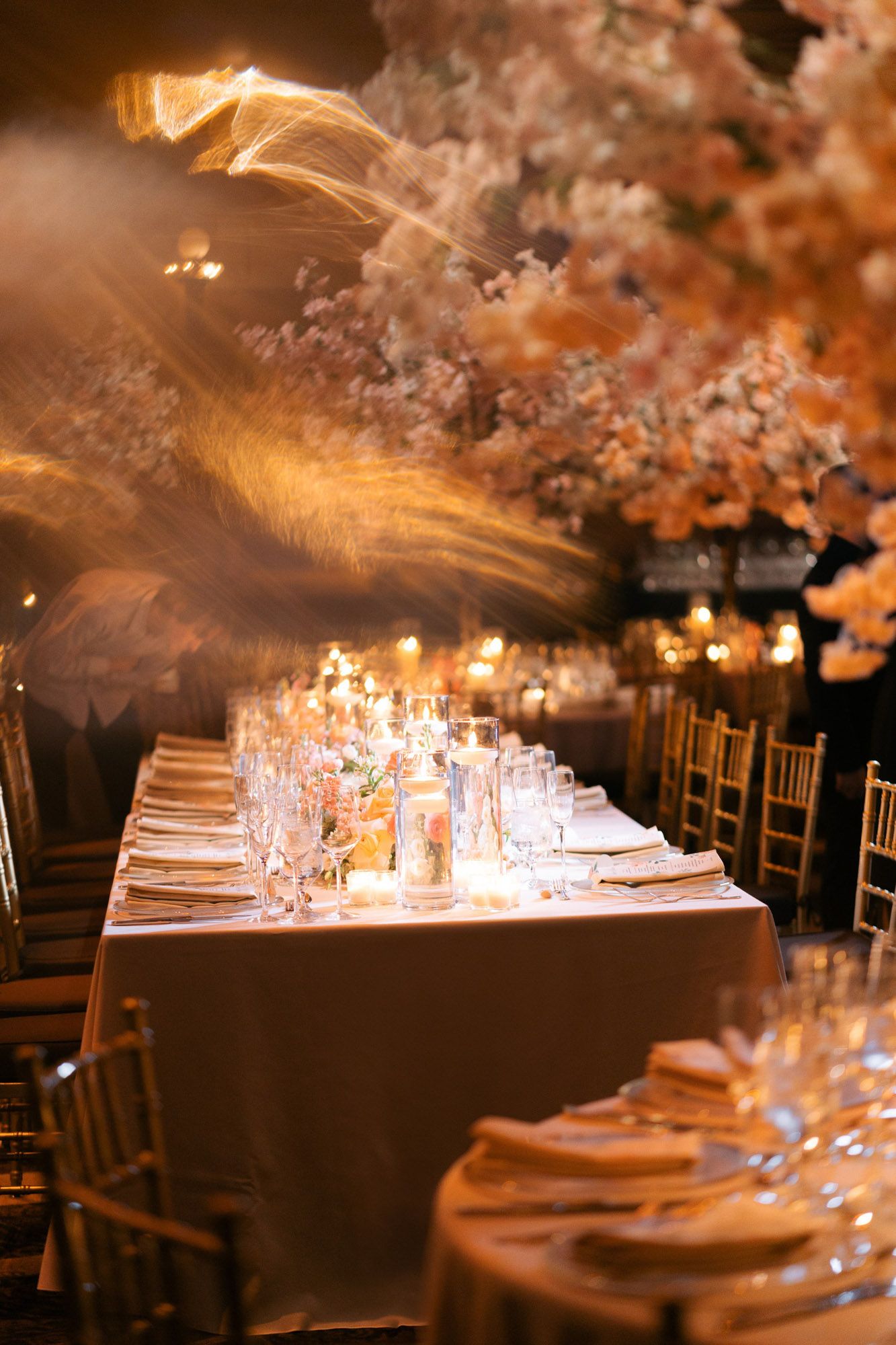 Elegant wedding reception table settings with glowing candles and place settings in a dimly lit banquet hall.