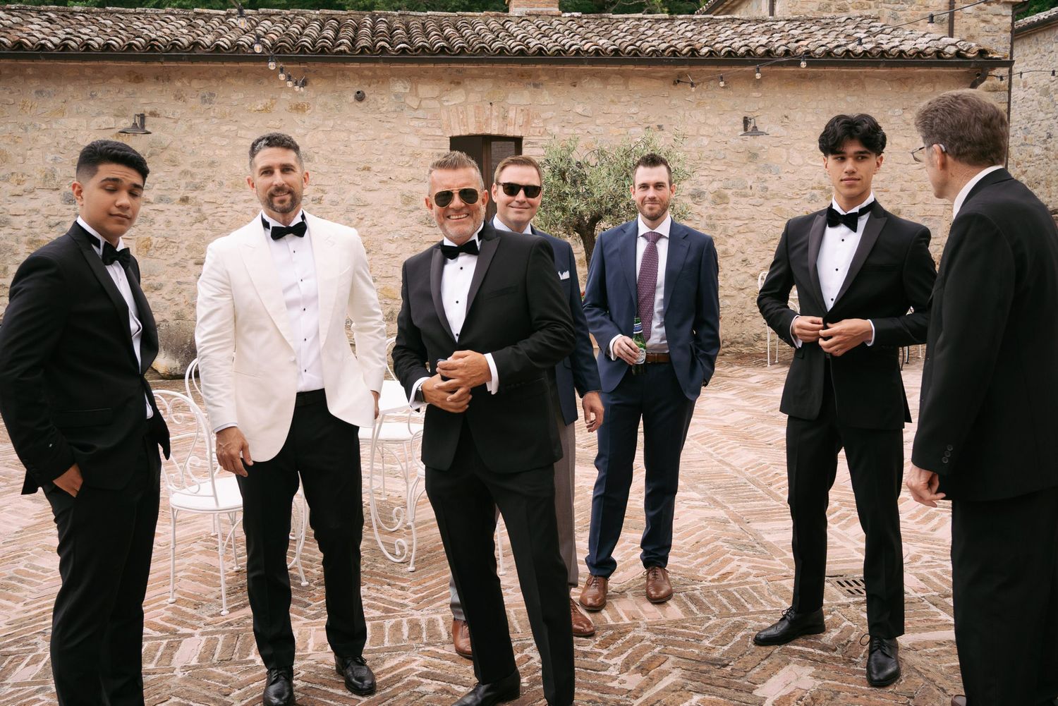 A panoramic view of groomsmen in black tuxedos and bow ties standing together at a wedding venue.