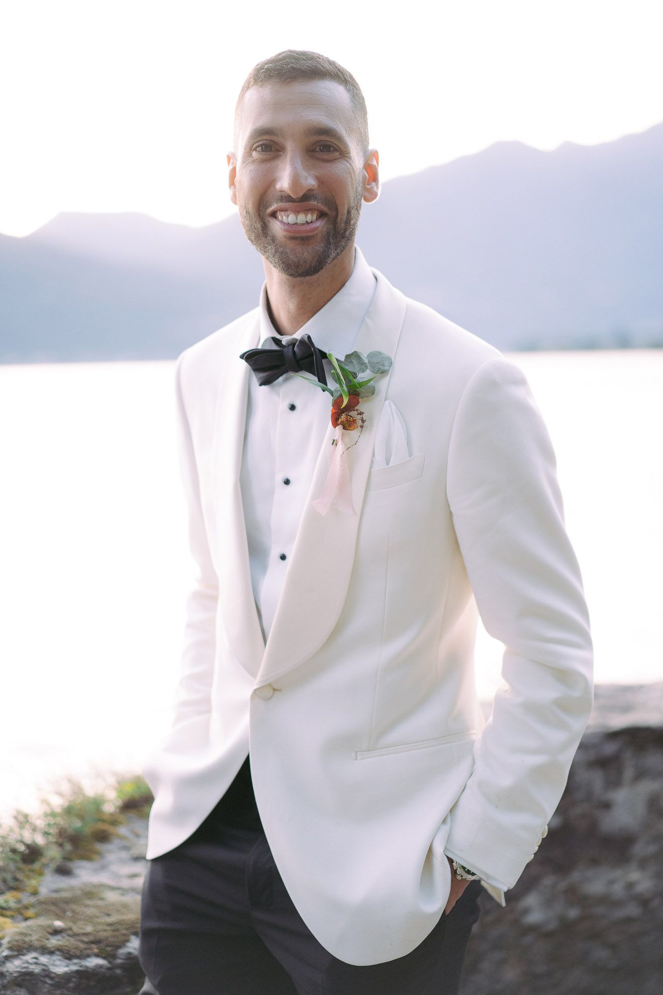 Three photos of a groom in a white tuxedo jacket and black bow tie posing outdoors with mountains in background.