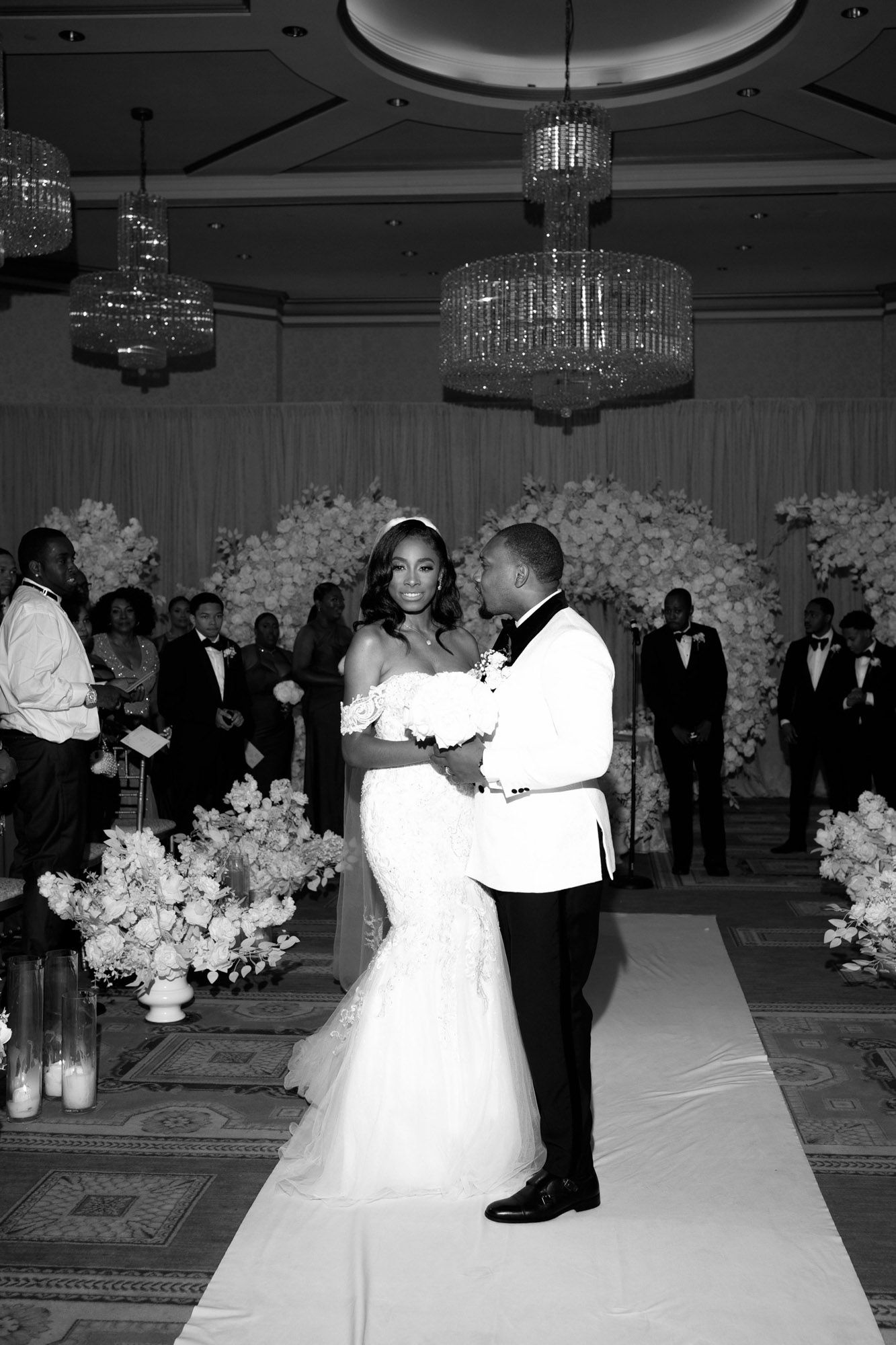 A black and white photo series showing couples dancing at an elegant wedding reception with crystal chandeliers and floral decor.