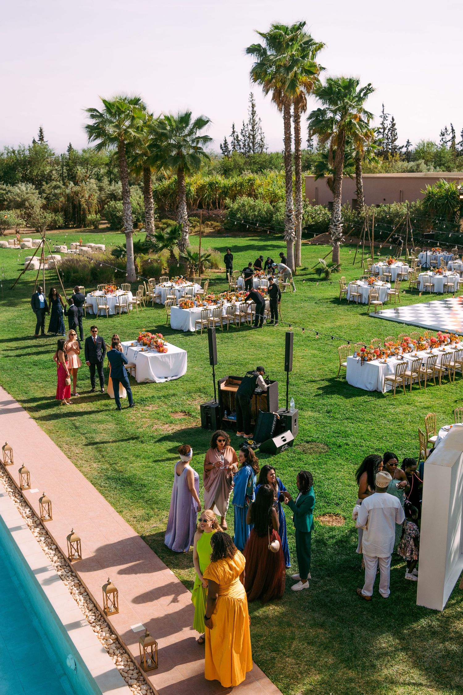 Garden wedding venue with guests mingling around decorated tables and palm trees.