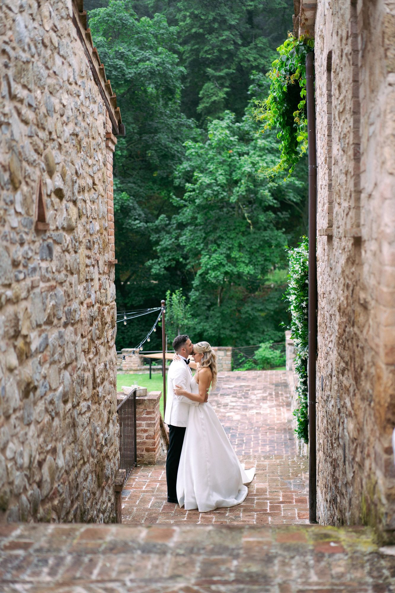 A romantic moment captured through stone archways at a historic venue surrounded by lush greenery.