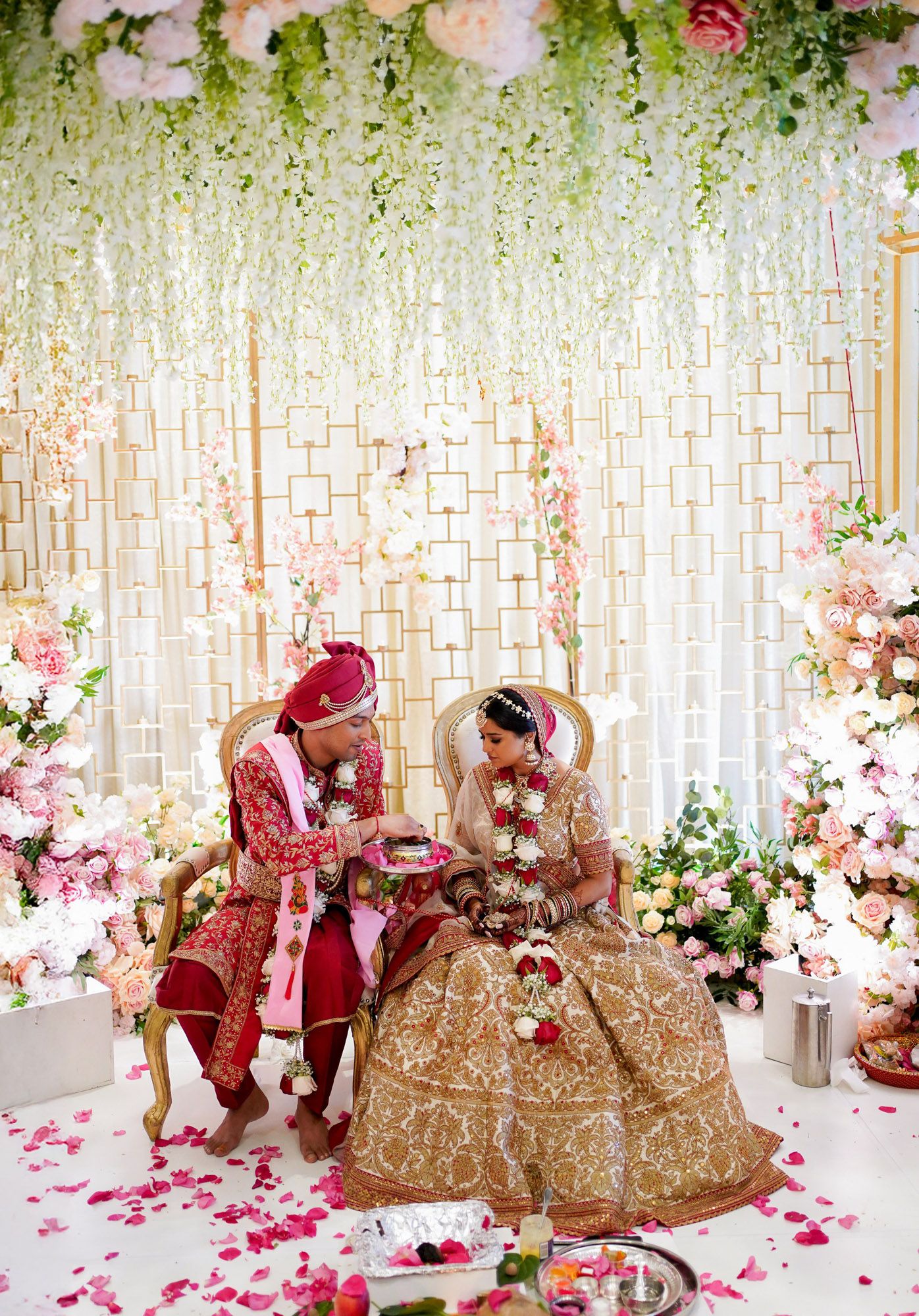 Elegant Indian wedding ceremony setup with floral decorations, pink and white roses, and ornate seating against a shimmering backdrop.
