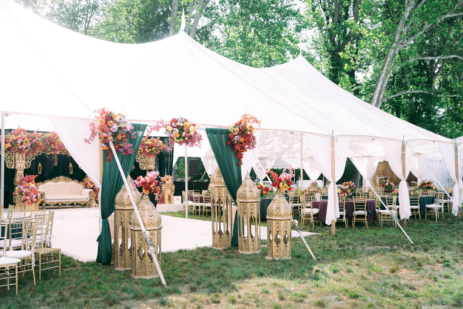 White wedding tent pavilions decorated with coral flowers create an elegant outdoor reception setting in a lush garden.