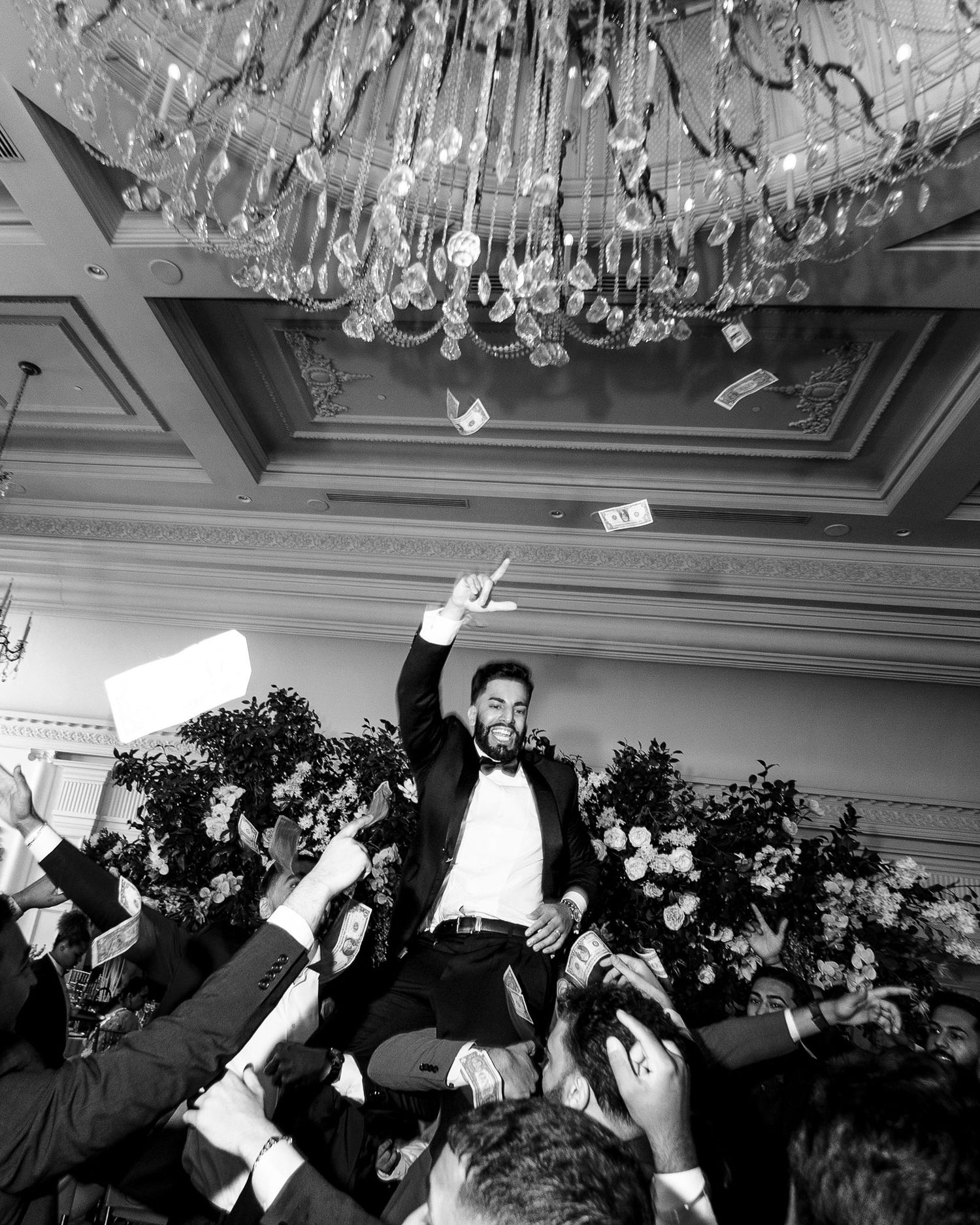 Black and white photo of guests tossing paper airplanes in celebration at an elegant ballroom reception.