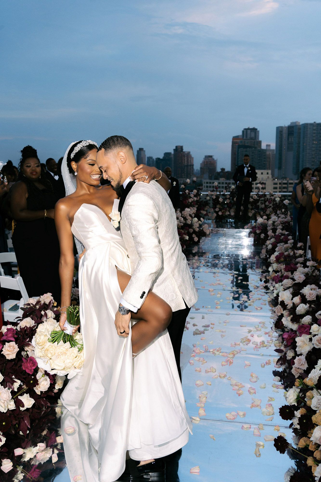 A romantic rooftop wedding ceremony with white decor and floral arrangements against a city skyline backdrop.