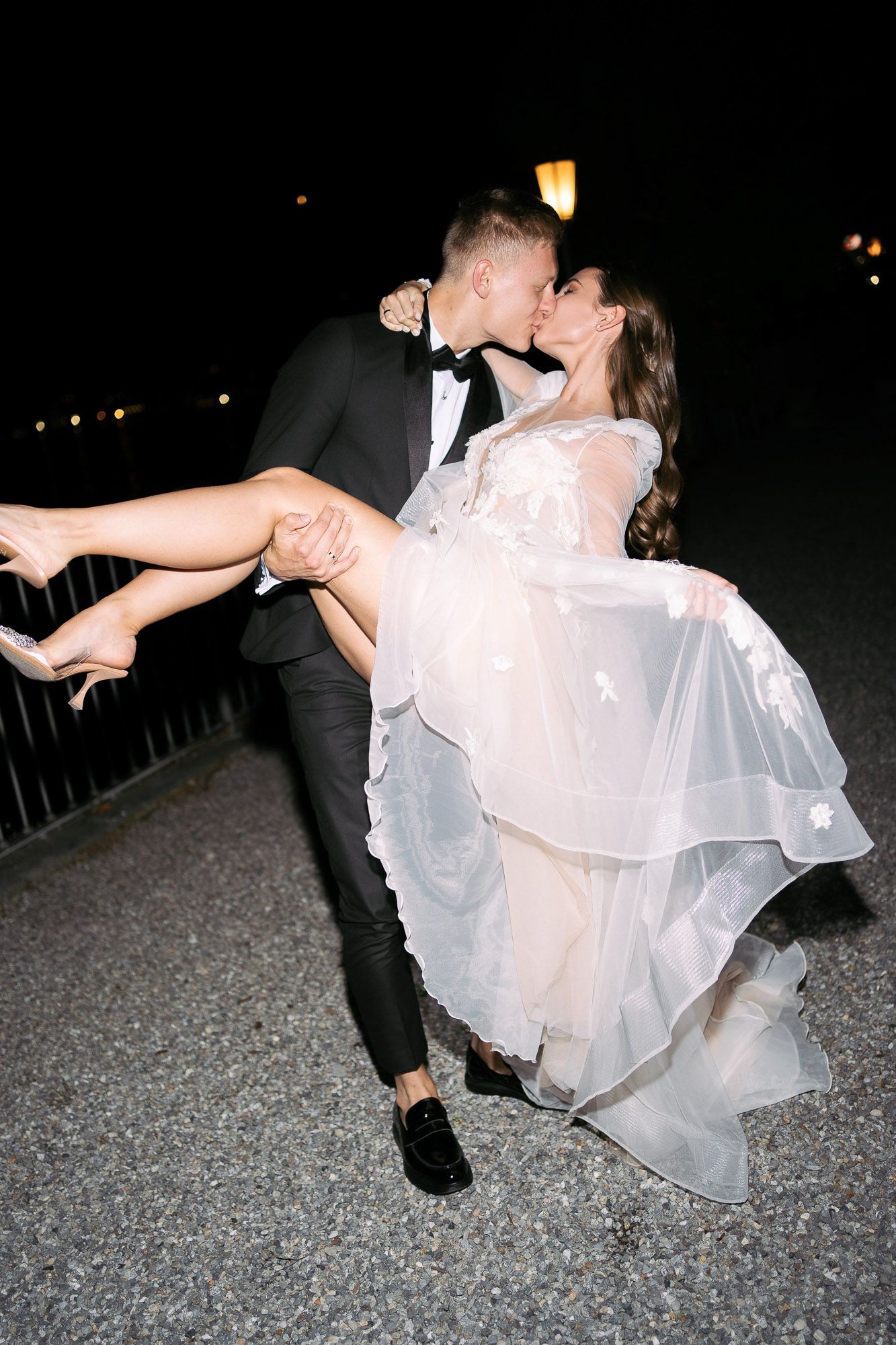 A romantic nighttime wedding photo shows a couple sharing a kiss while the groom dips the bride in her flowing white dress.