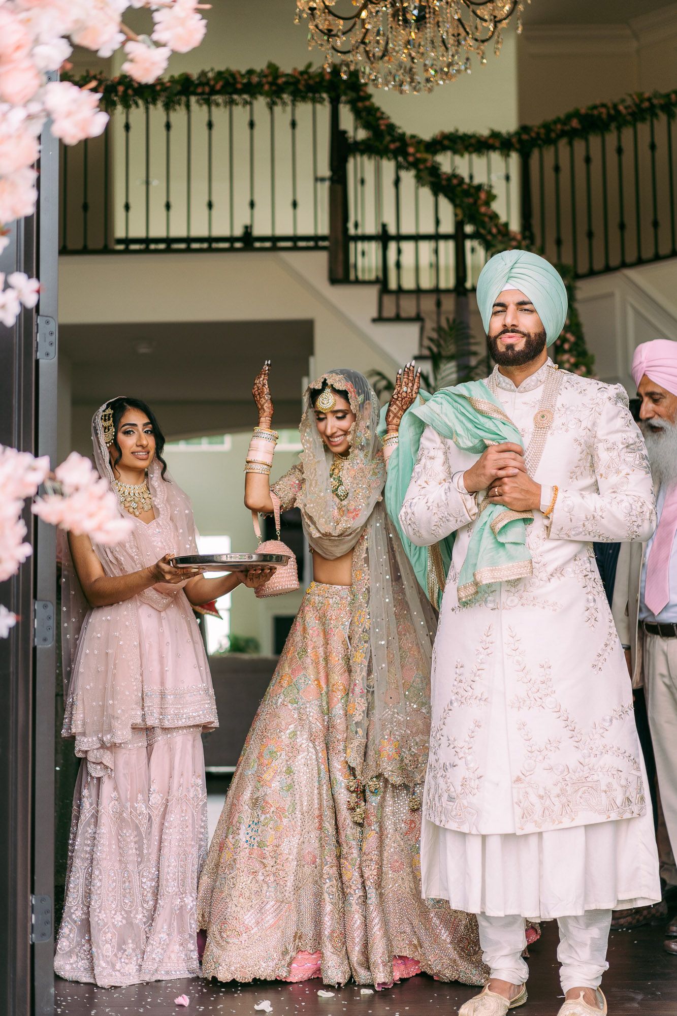 Wedding party celebrates in traditional South Asian attire with ornate pink and cream colored outfits at an elegant venue.