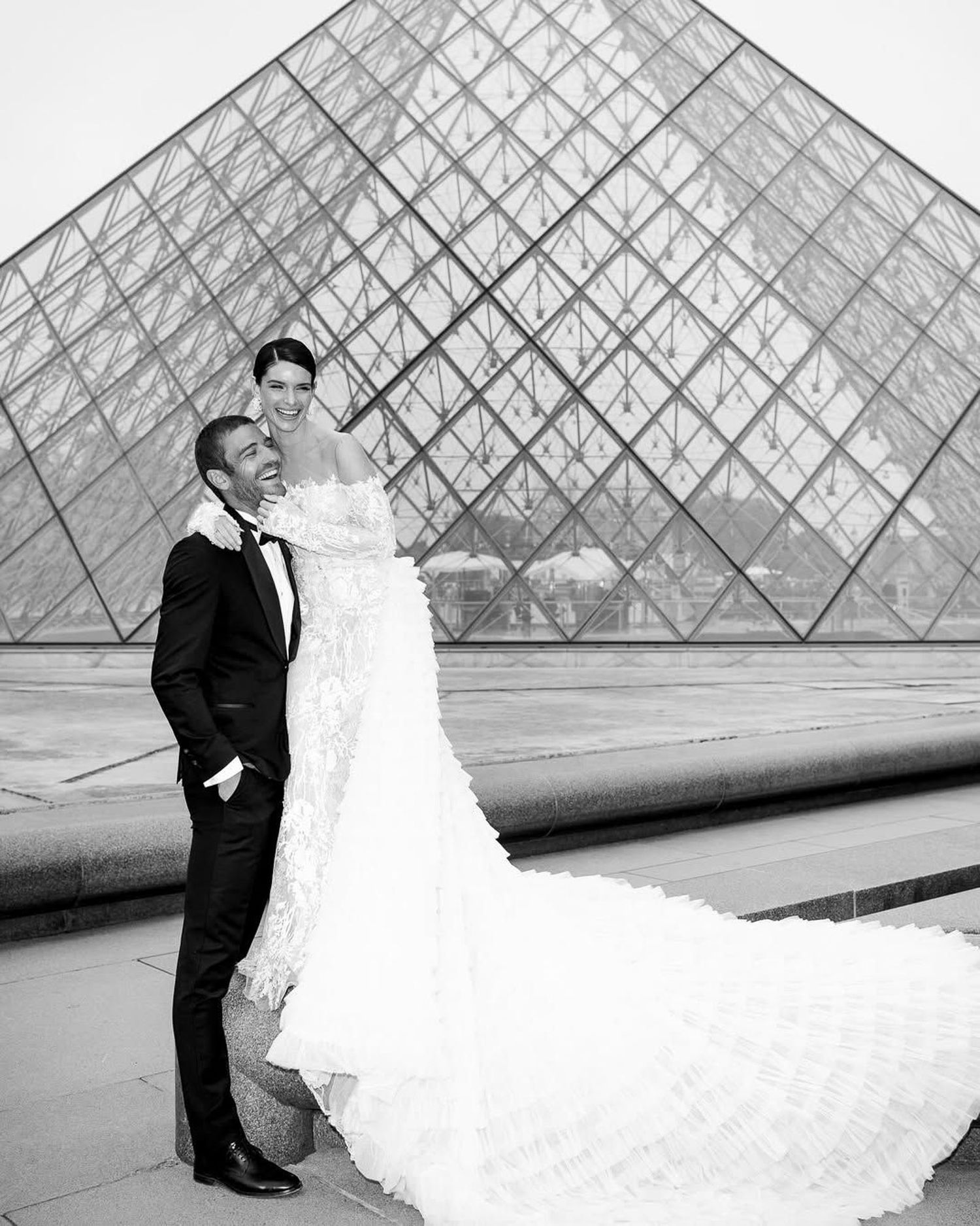 A couple poses for romantic black and white wedding photos in front of the iconic glass Louvre pyramid in Paris. wedding photographer