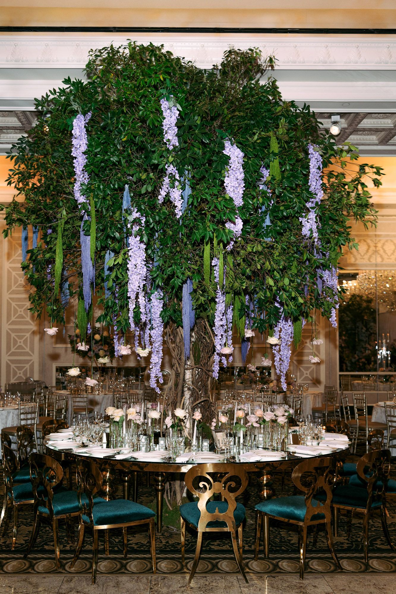 Elegant wedding reception table setup with hanging wisteria and greenery centerpiece above formal place settings.