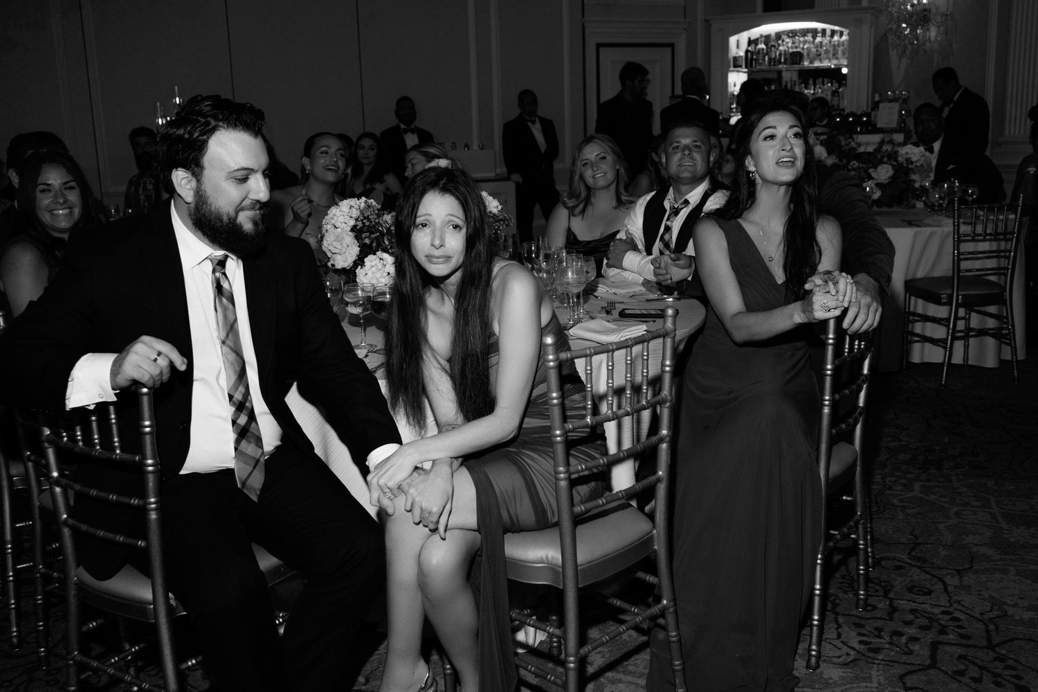 Black and white photo of wedding guests enjoying themselves at an elegant reception venue with chiavari chairs.