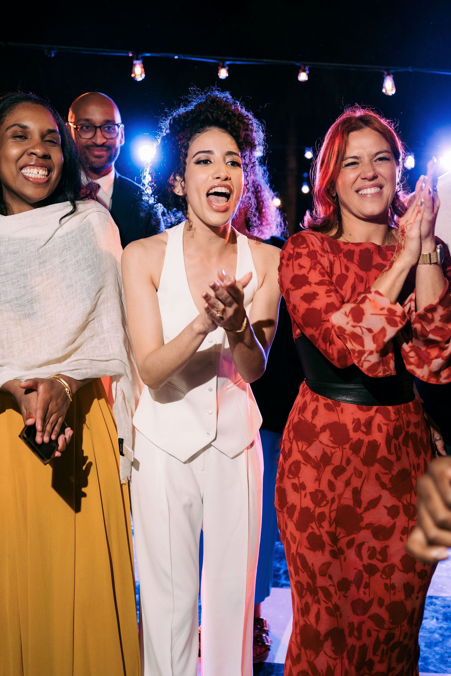 Wedding party celebrating on dance floor with colorful lighting and joyful expressions.