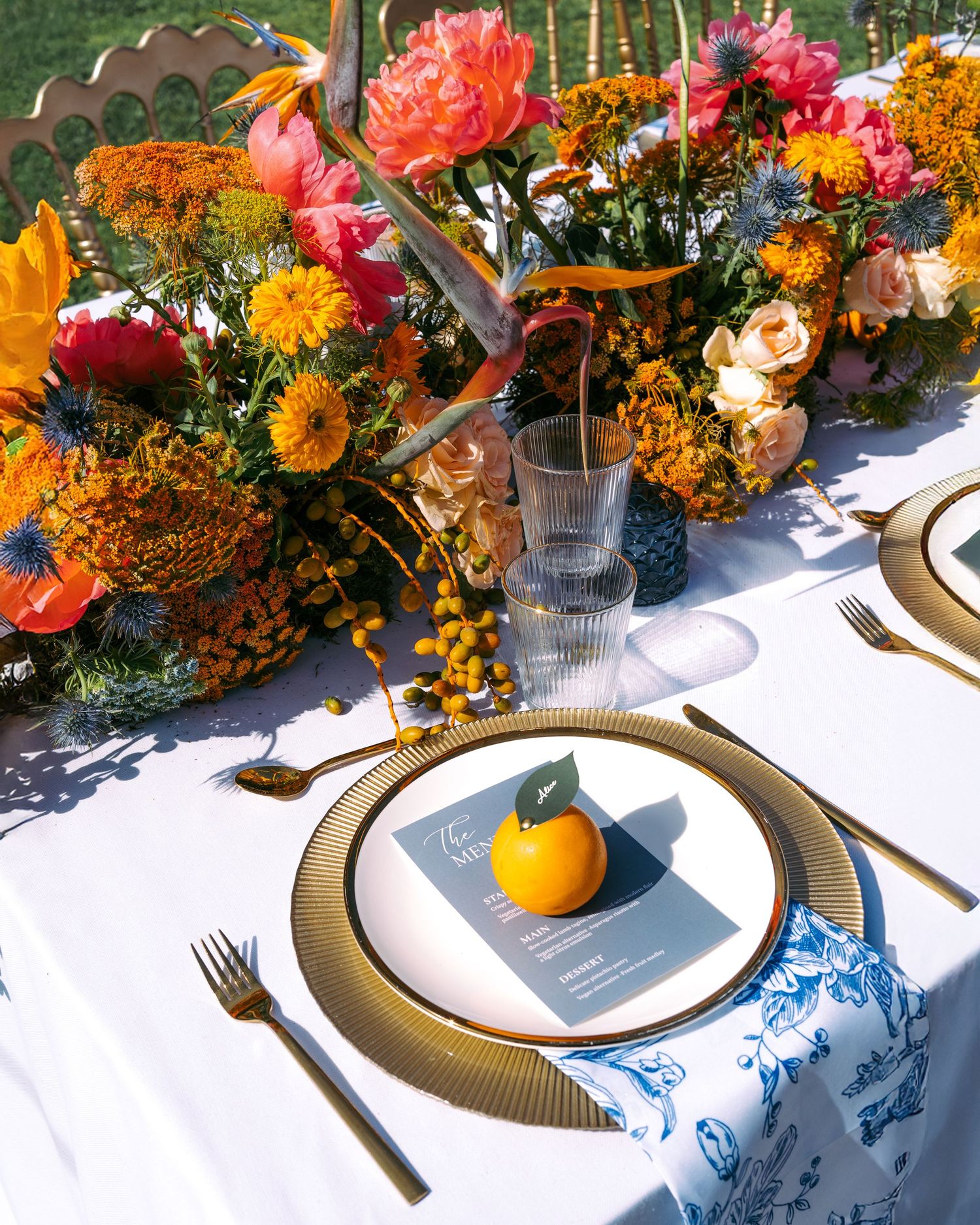 Vibrant table setting with colorful floral arrangements and citrus decor on white tablecloth.