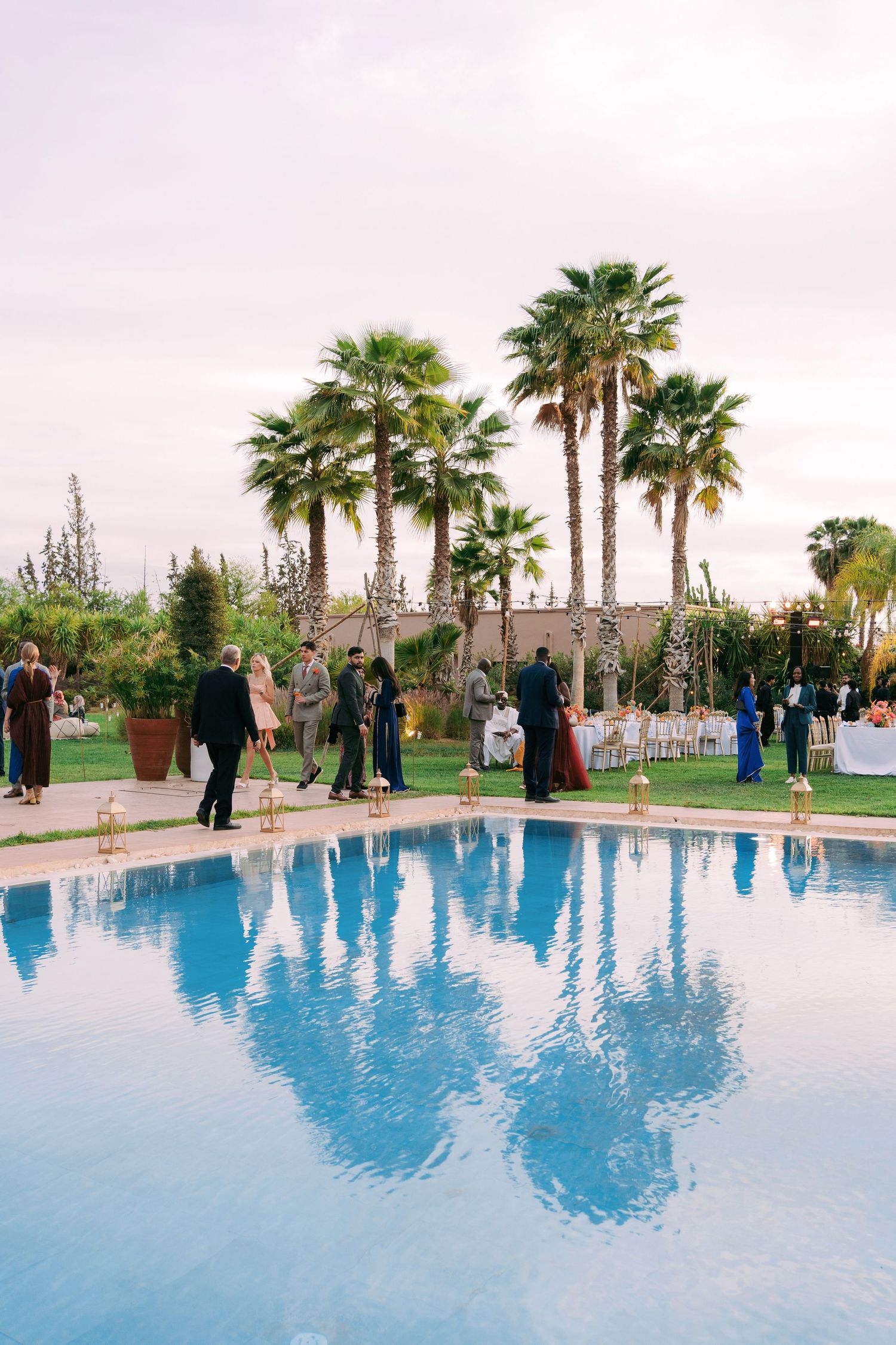 Wedding reception by luxurious pool with palm trees at sunset.