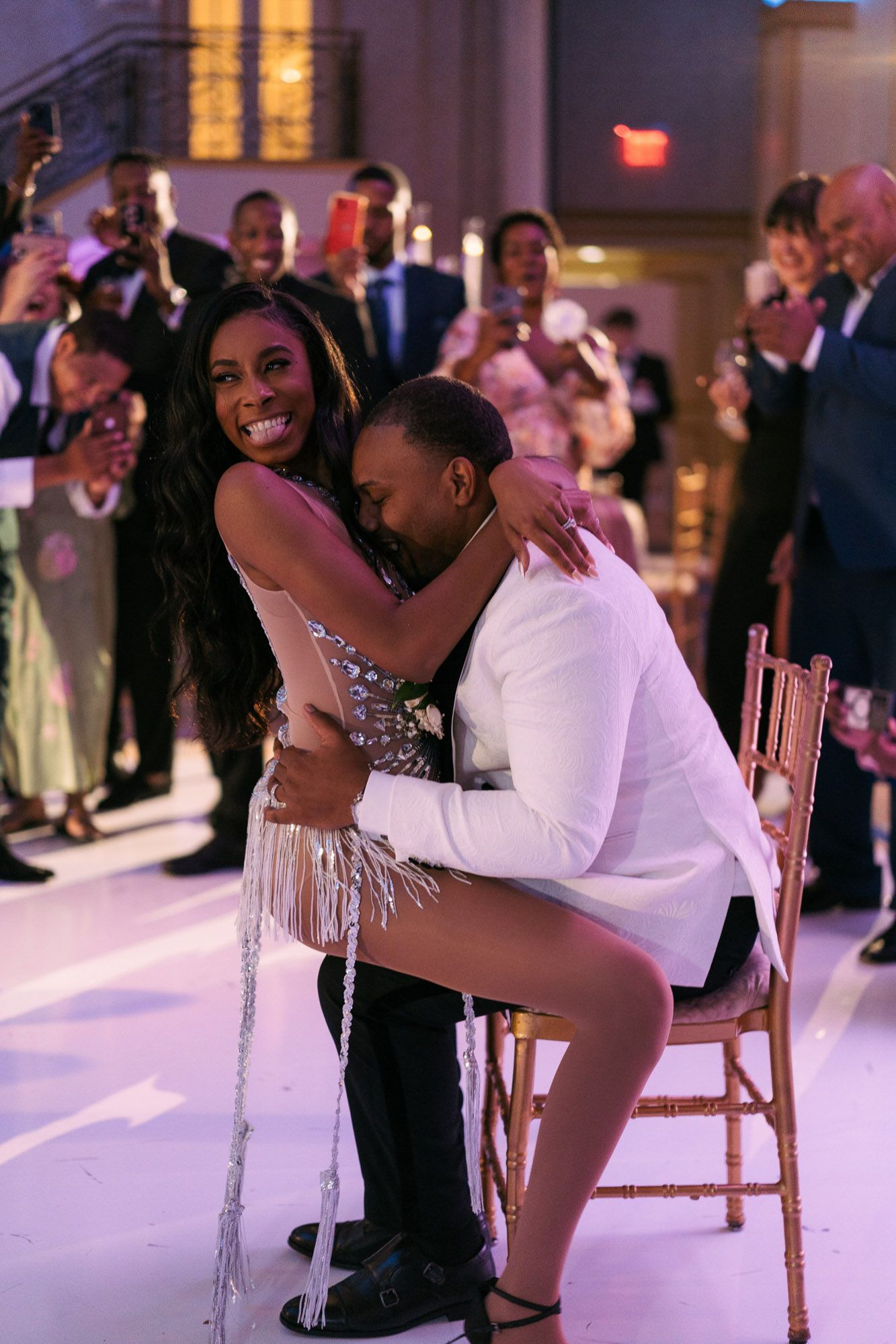 A couple shares an intimate dance moment at a wedding reception with guests watching in the background.