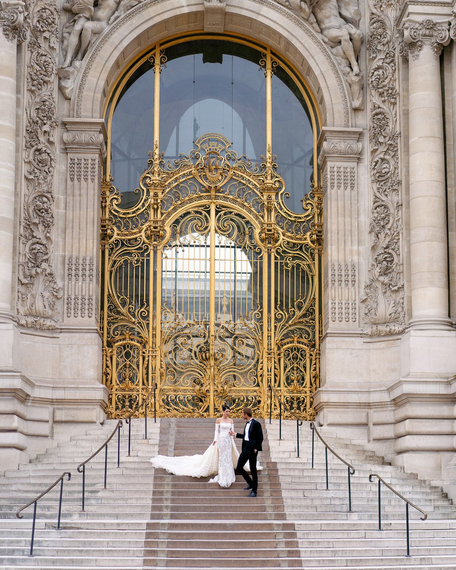 A couple poses on ornate marble steps with gilded gates at the Petit Palais in Paris, creating elegant wedding photos.
