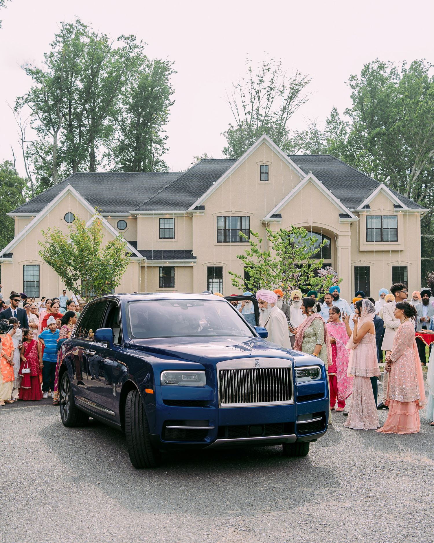 A luxurious blue Rolls-Royce parked at an outdoor event with guests gathered around in formal attire.