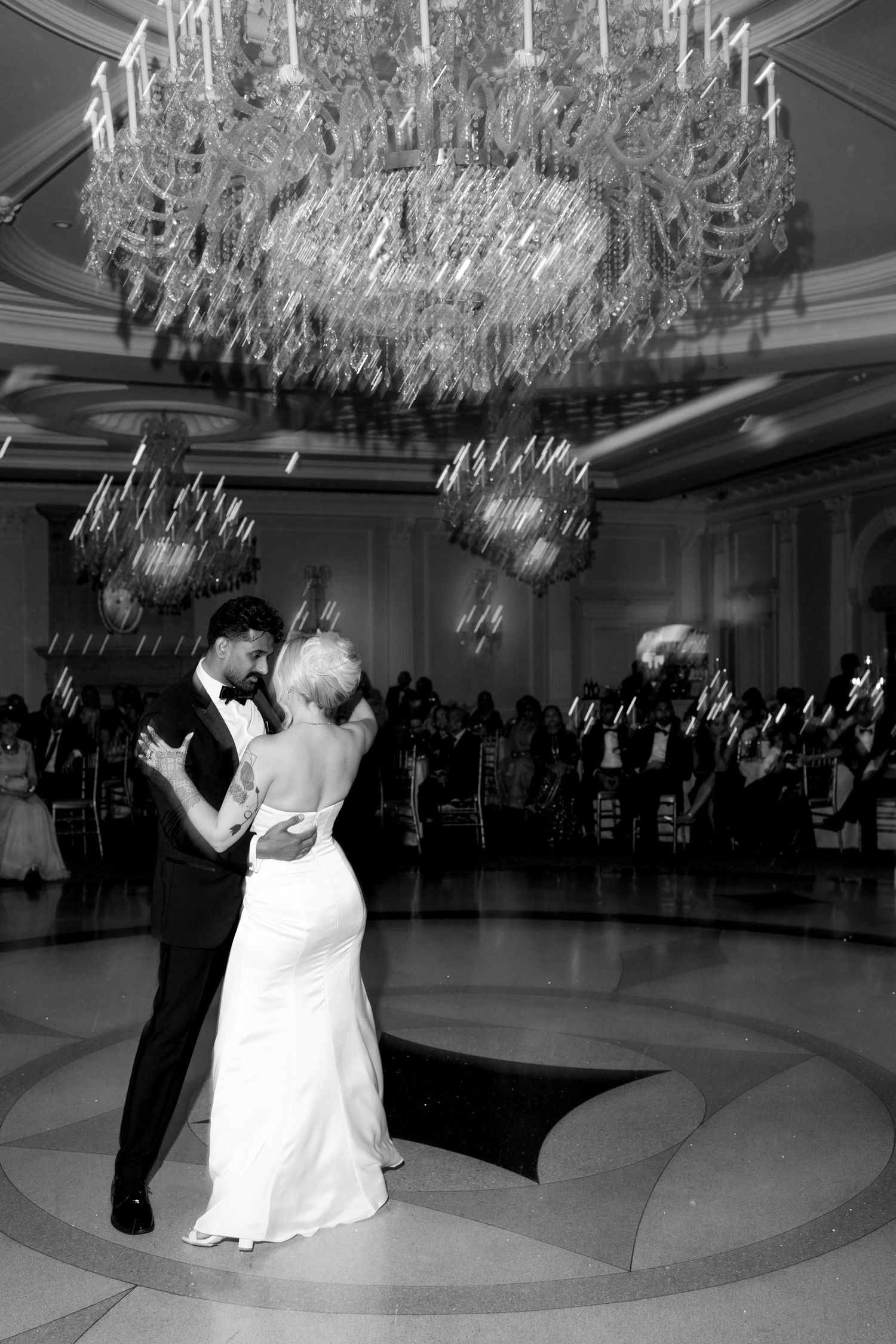 Black and white capture of a dance under an elaborate crystal chandelier at an elegant wedding reception.