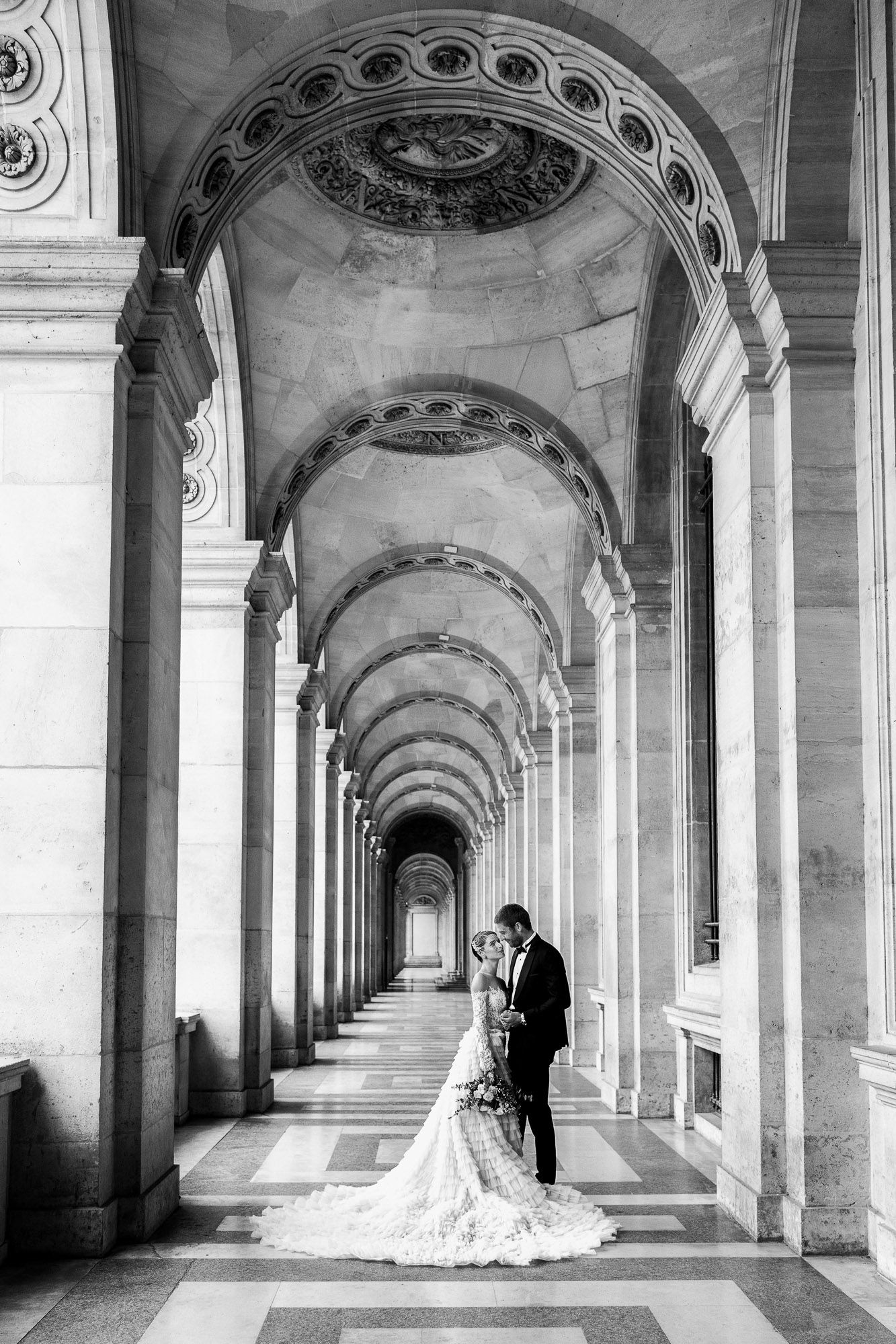 A stunning black and white wedding photo series captured under ornate arched corridors with dramatic lighting and shadows.