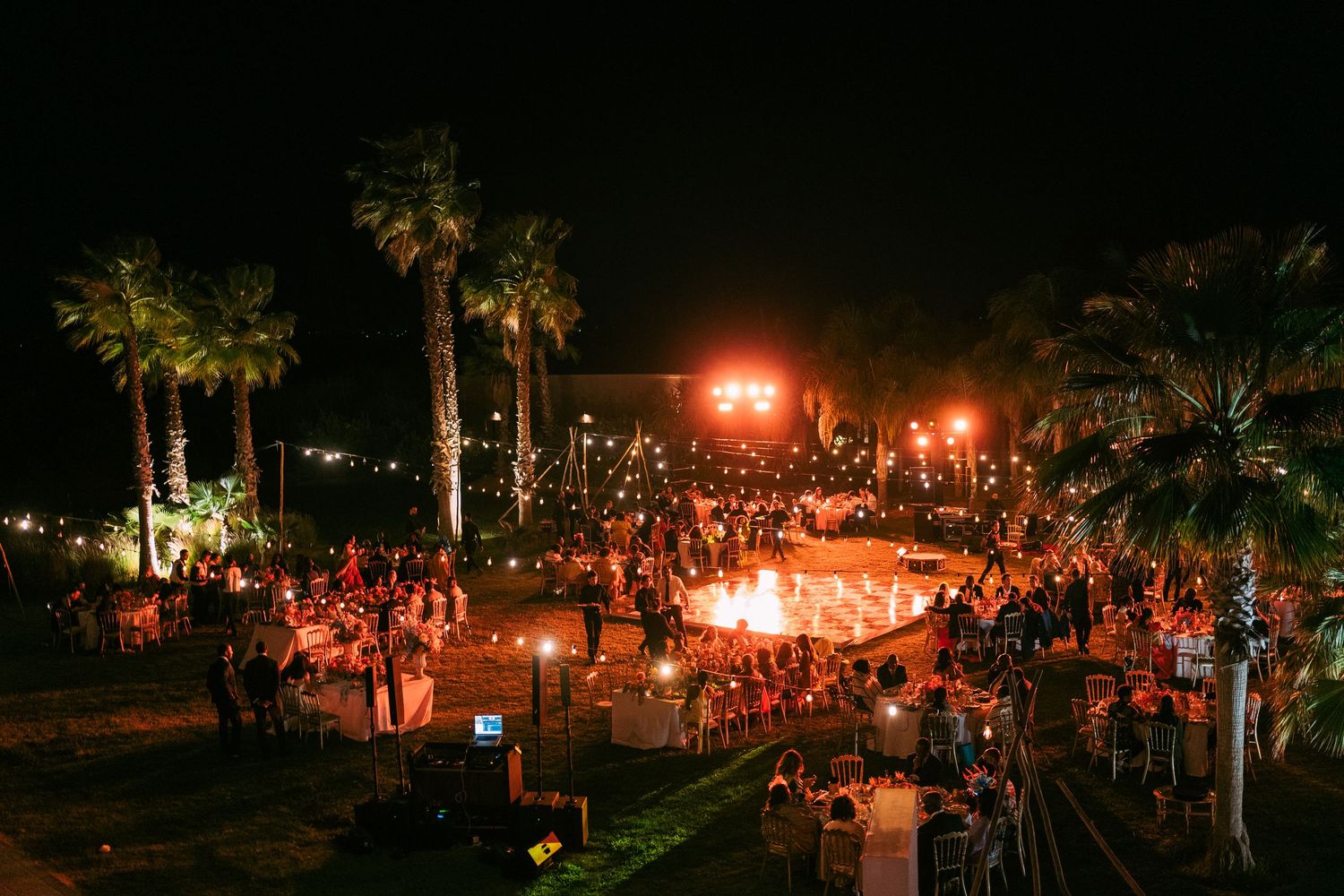 Night wedding reception under string lights with palm trees creating a magical outdoor ambiance.