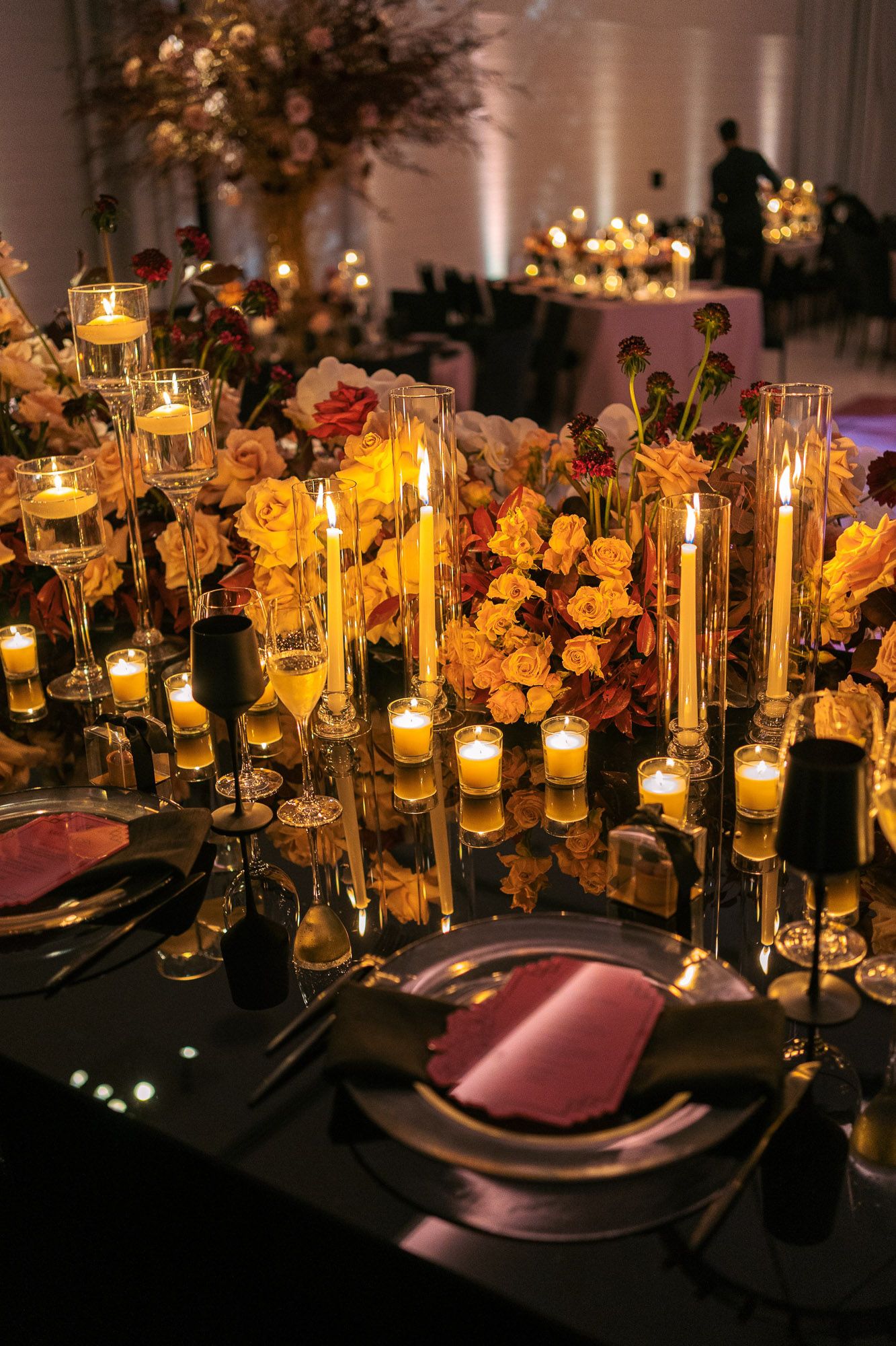 Elegant wedding table setting with glowing candles, yellow roses and black tablecloth creating romantic ambiance.