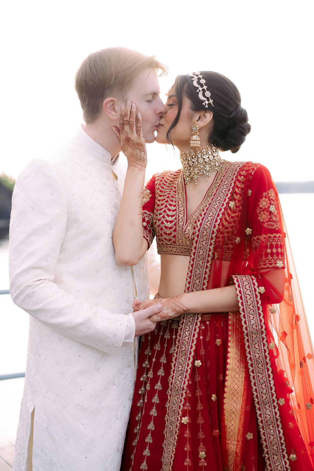 A sequence of romantic moments between a couple in white and red traditional Indian wedding outfits.
