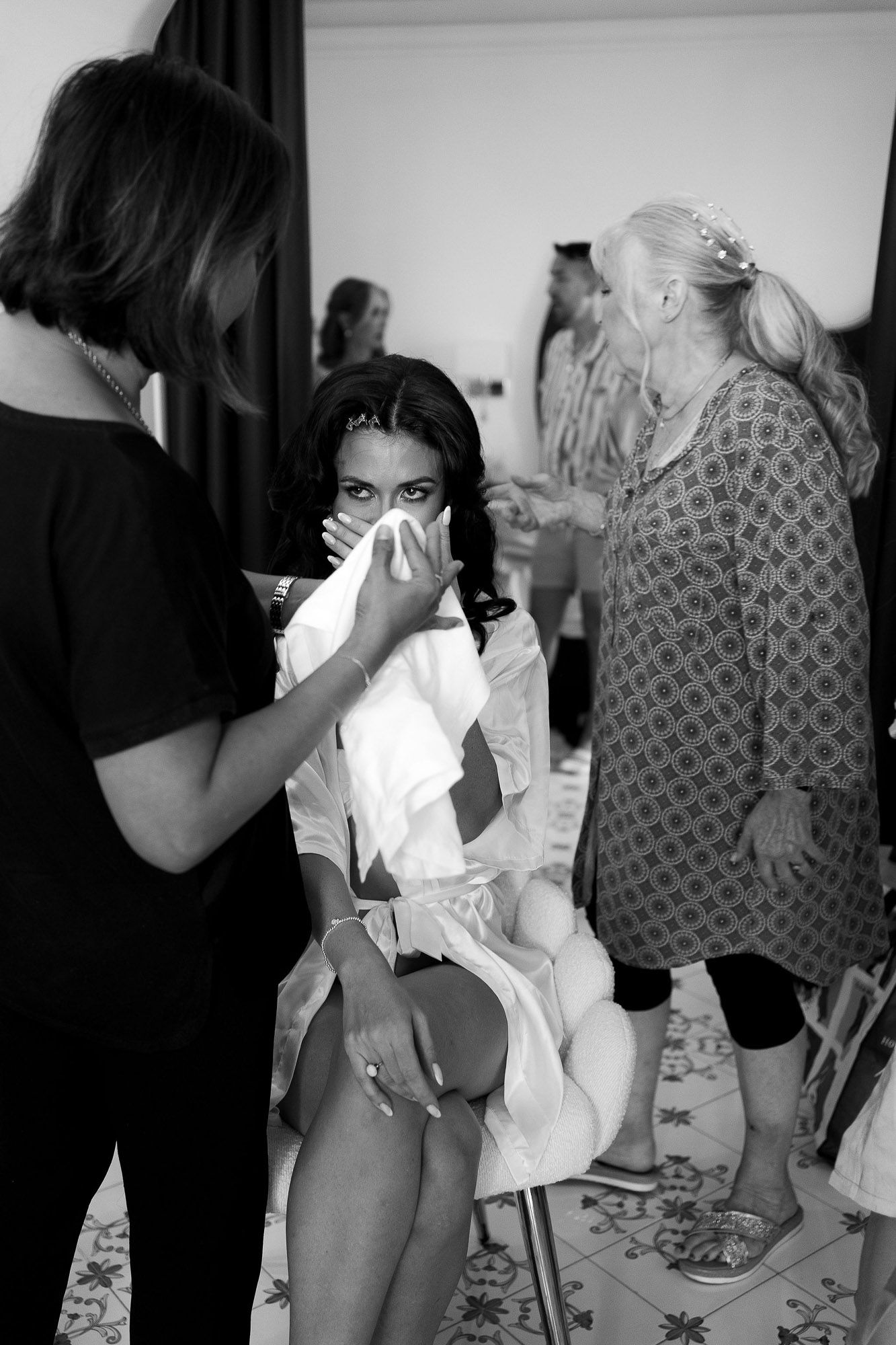 Behind-the-scenes fashion photoshoot showing models getting ready in a dressing room with stylists and clothing racks.