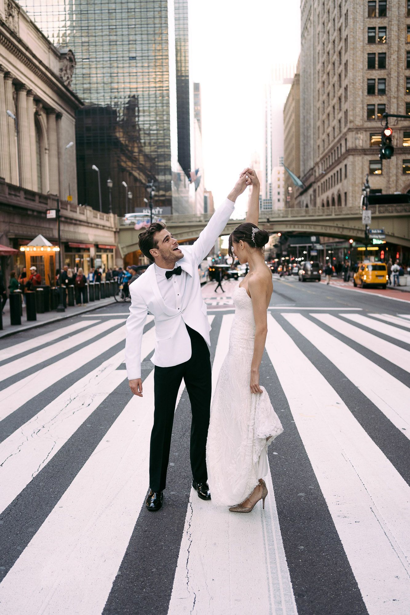 A couple dances and poses together on a zebra crossing in downtown New York City with skyscrapers in the background.