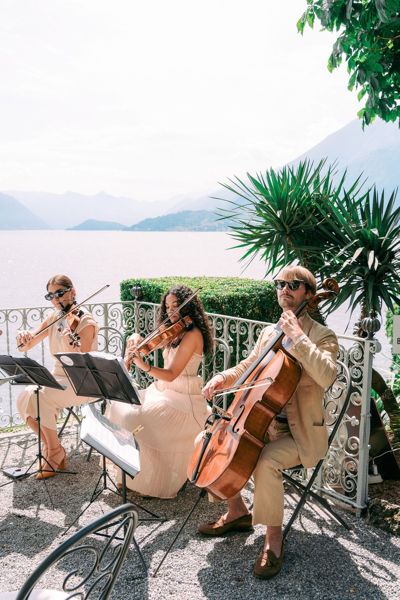 Musicians perform classical music on string instruments on an elegant terrace overlooking a scenic landscape.
