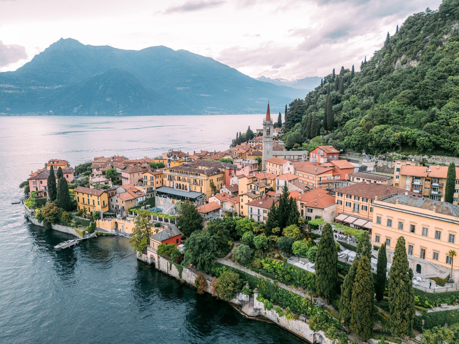 Scenic panoramic view of Varenna town with colorful buildings along Lake Como's shoreline in Italy on a cloudy day.