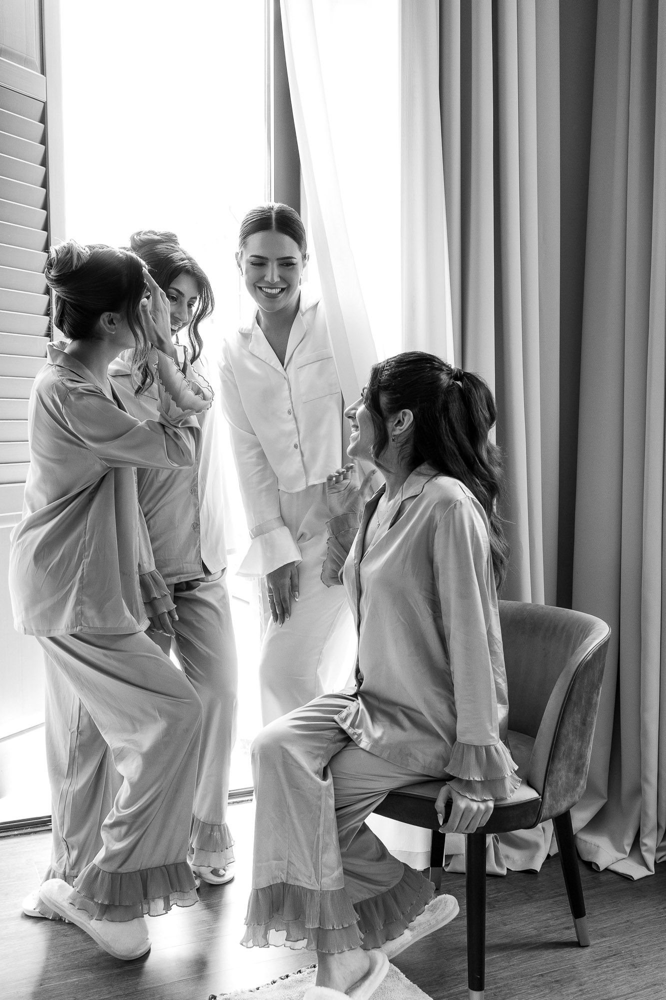 A candid moment of friends in matching white sleepwear sharing a joyful conversation by a window.