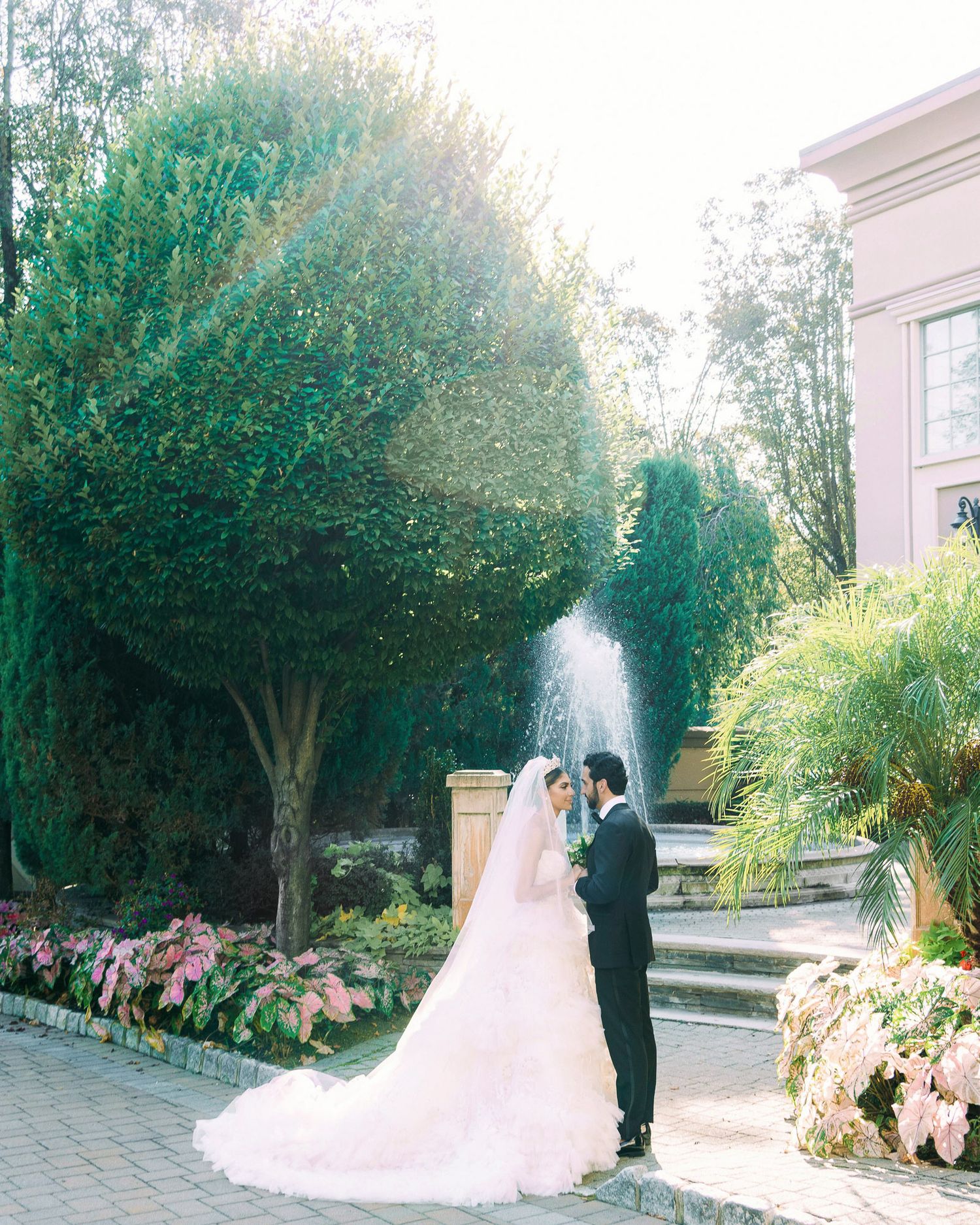 A romantic wedding couple poses together in a lush garden setting with blooming flowers and greenery.