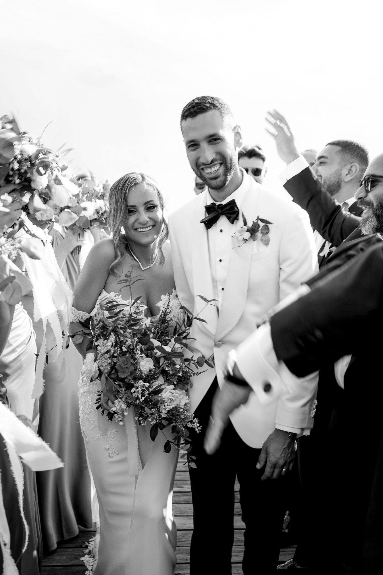 A black and white wedding photo showing a joyful couple walking down the aisle with guests celebrating around them.
