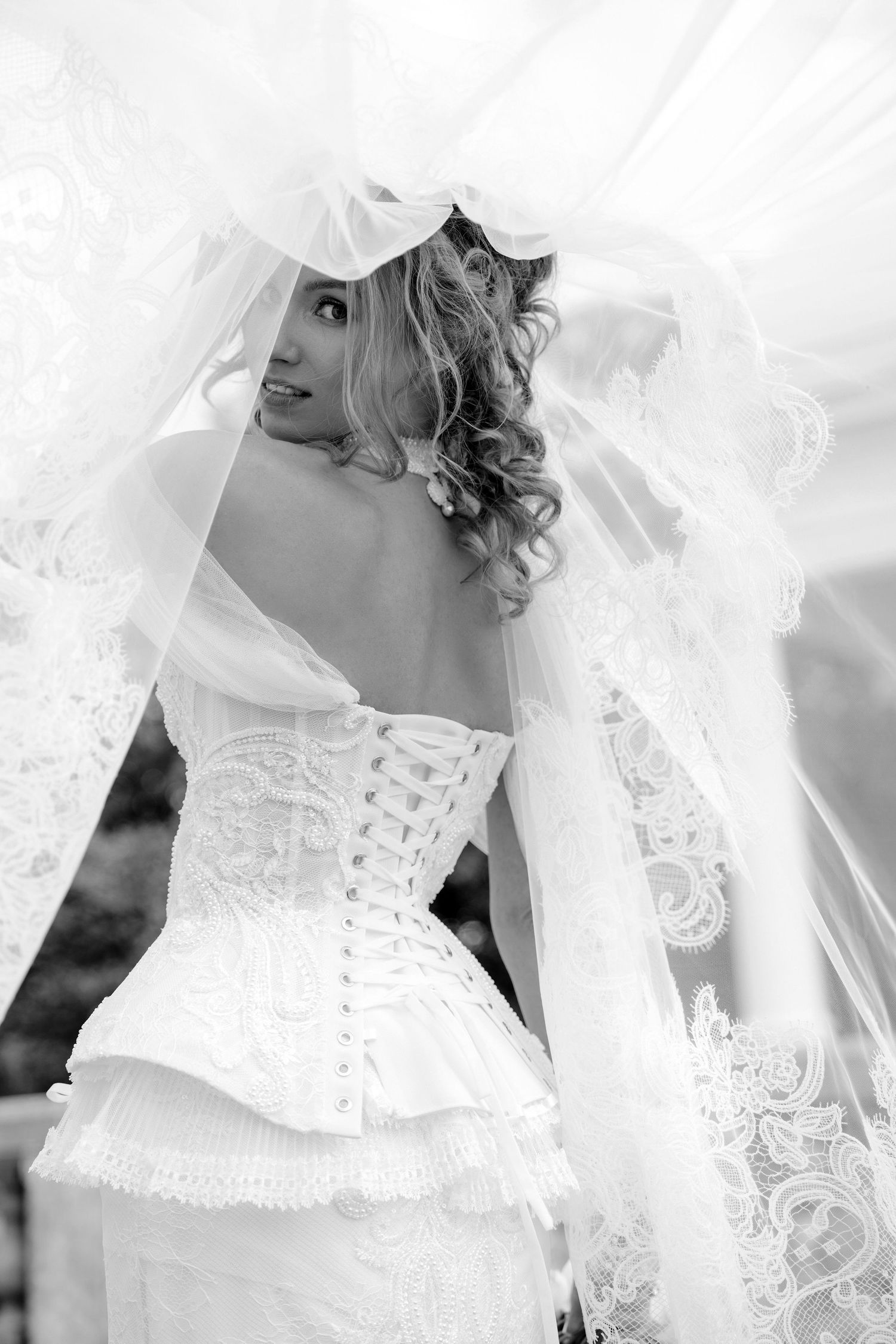 Black and white close-up photo of a bride in a lace wedding dress with delicate details and veil.