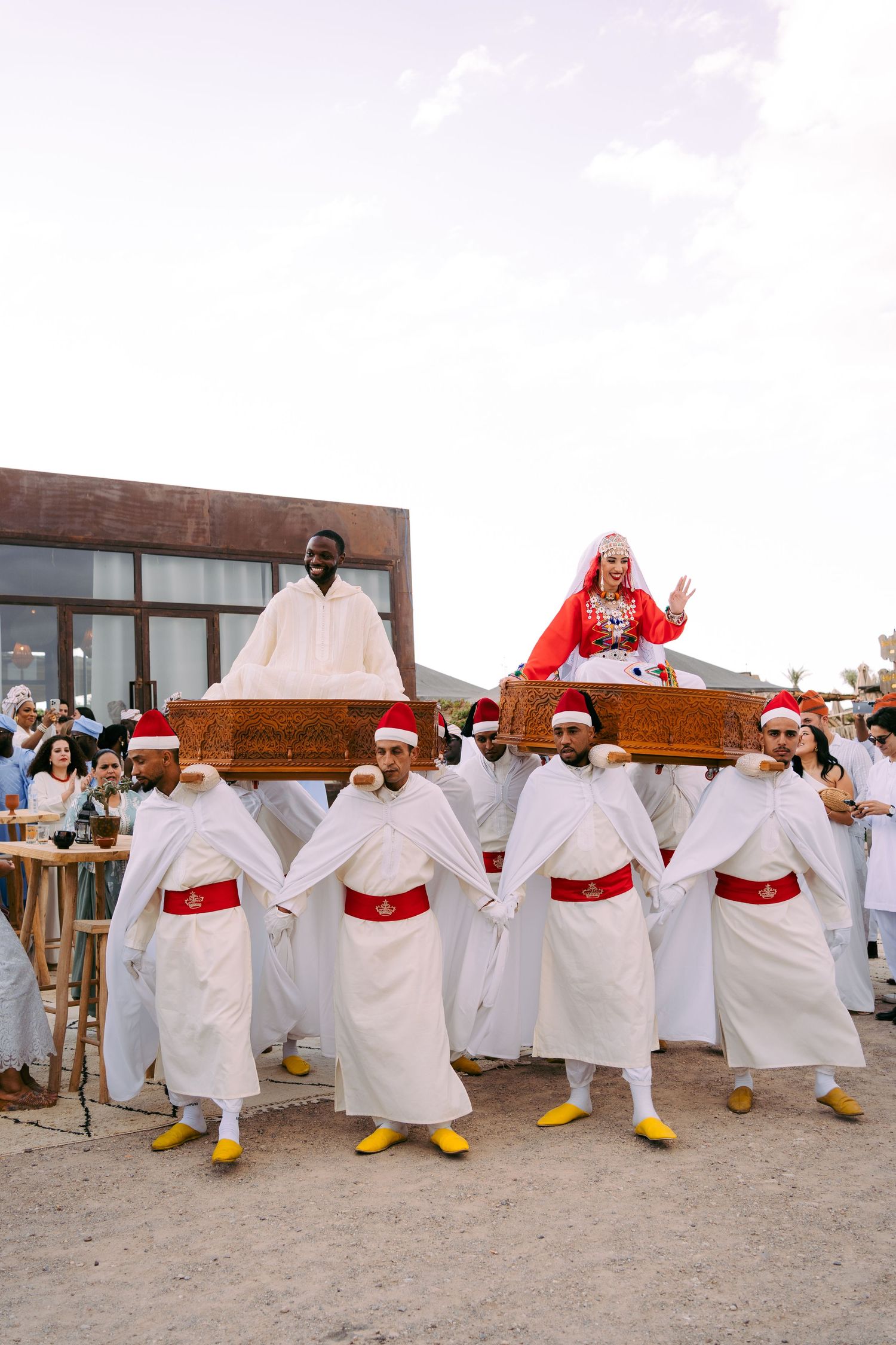 A group performing a festive dance routine wearing matching white outfits with red sashes and yellow boots.