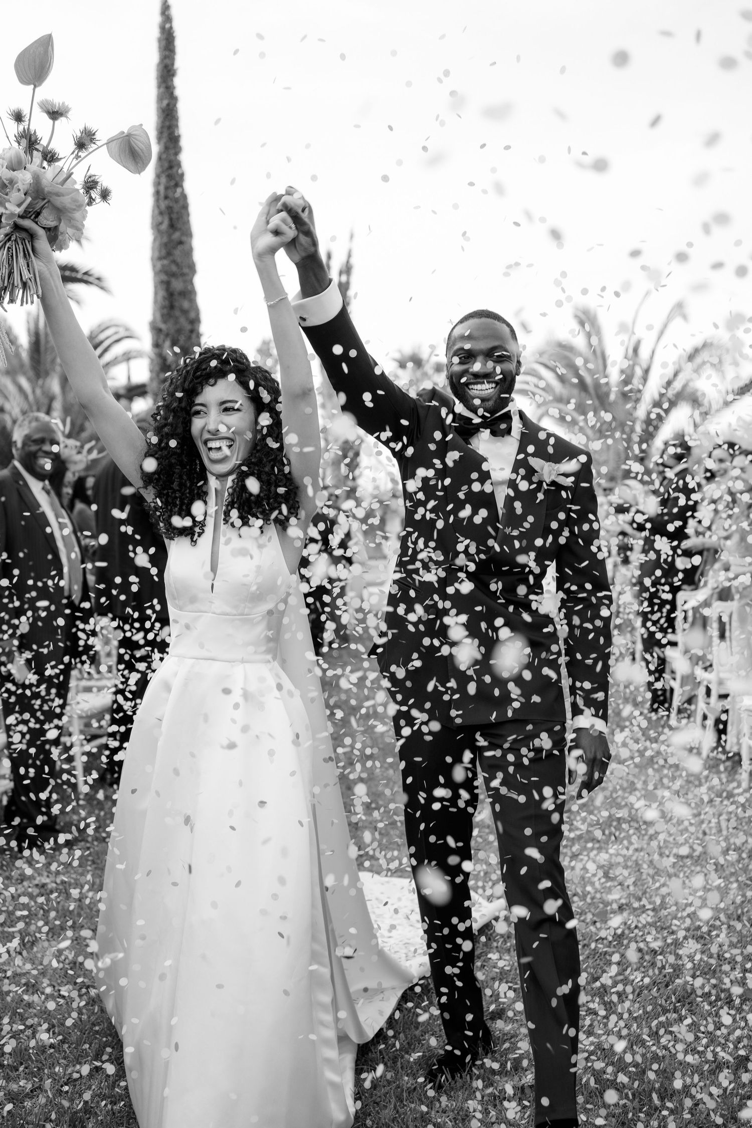 Wedding celebration moment captured in black and white with confetti falling during an outdoor ceremony.