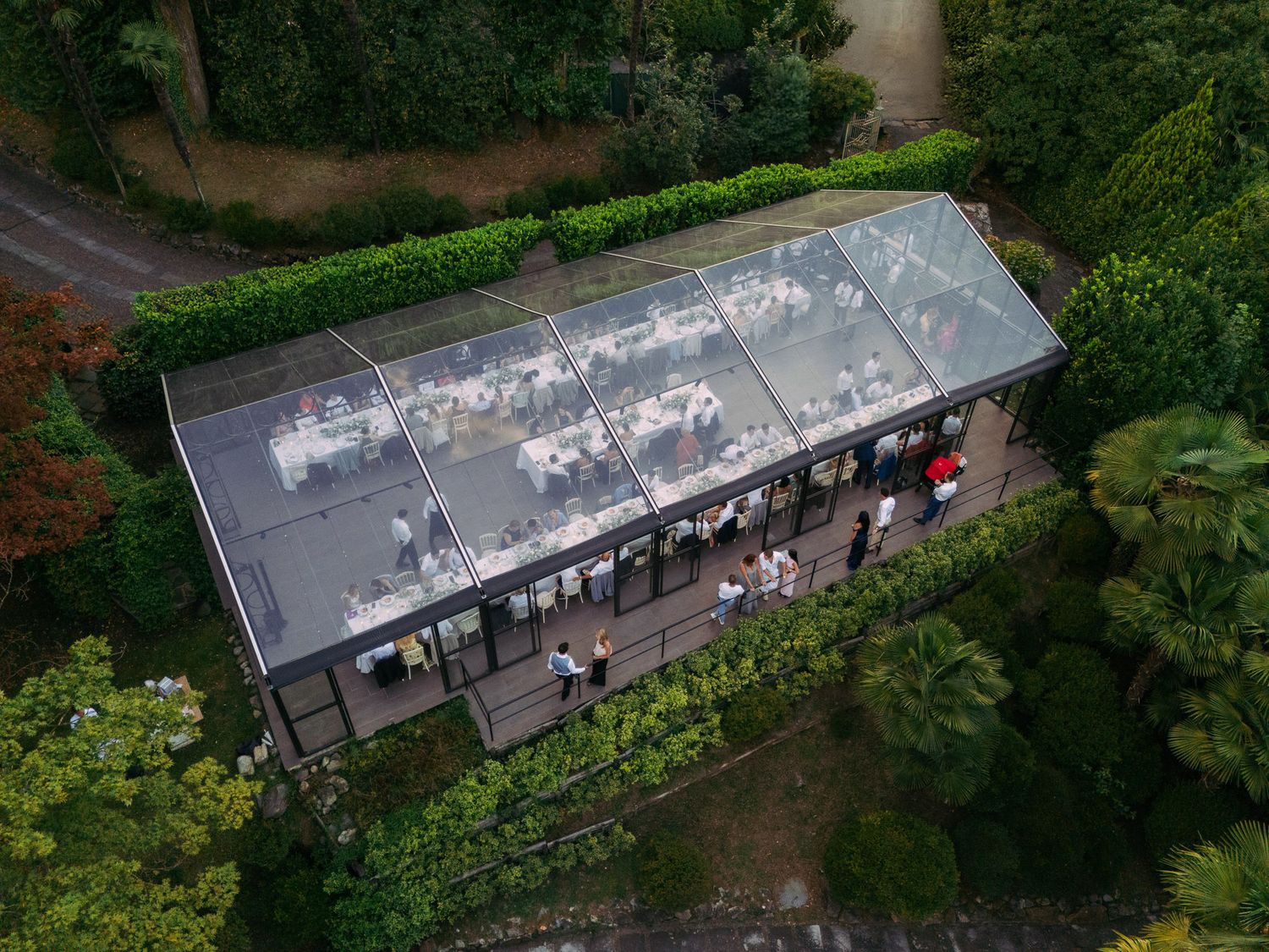 Aerial view of a glass-roofed greenhouse or conservatory surrounded by lush green gardens.